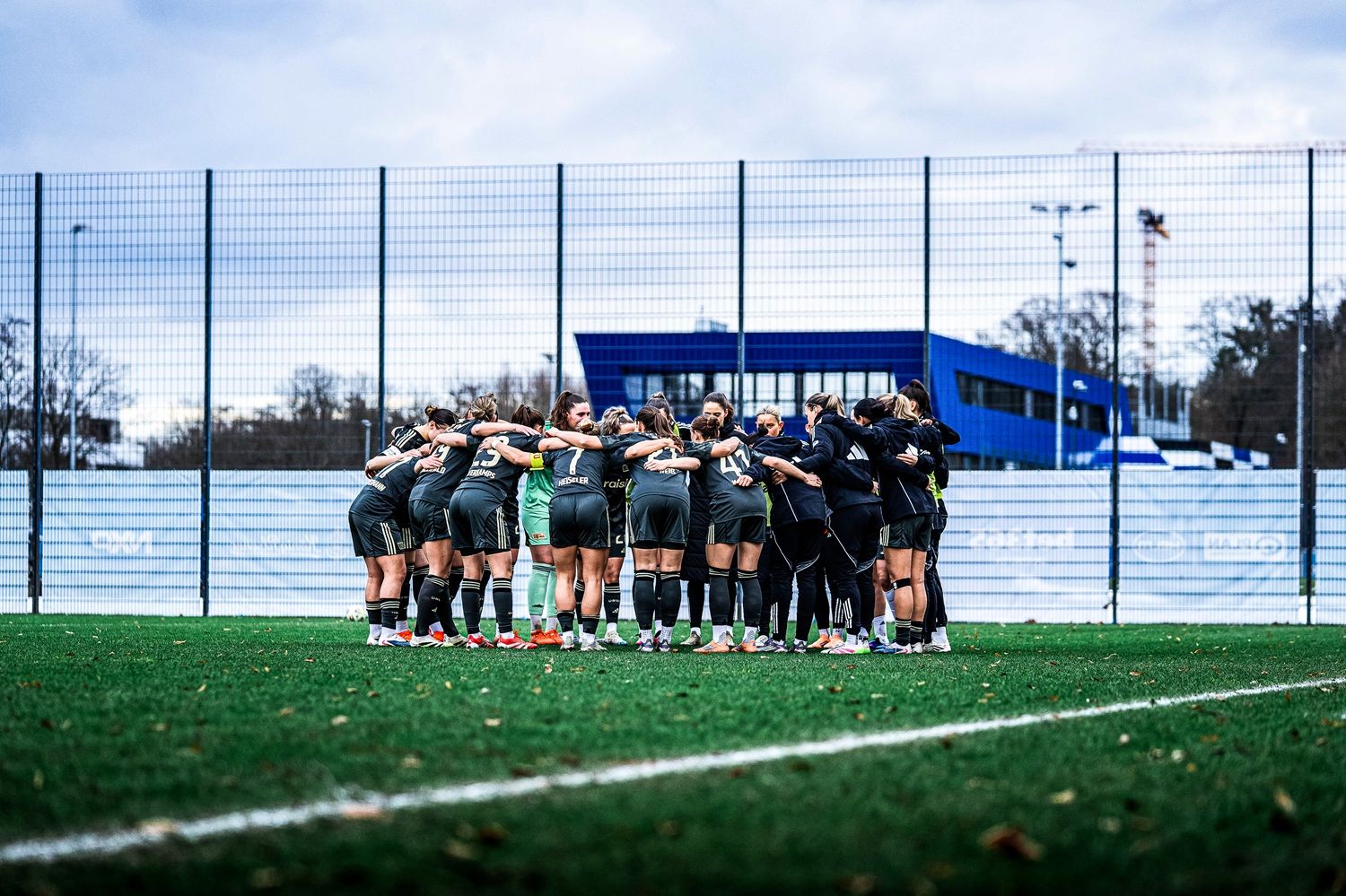 Zwei Gruppen von Fußballspielerinnen umarmen sich auf einem Sportplatz vor einem Training oder einem Spiel.