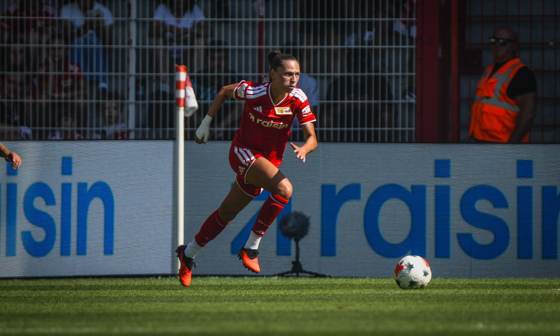 Eine Fußballspielerin in rot läuft im Stadion auf den Ball zu, während sie eine Eckfahne passiert.