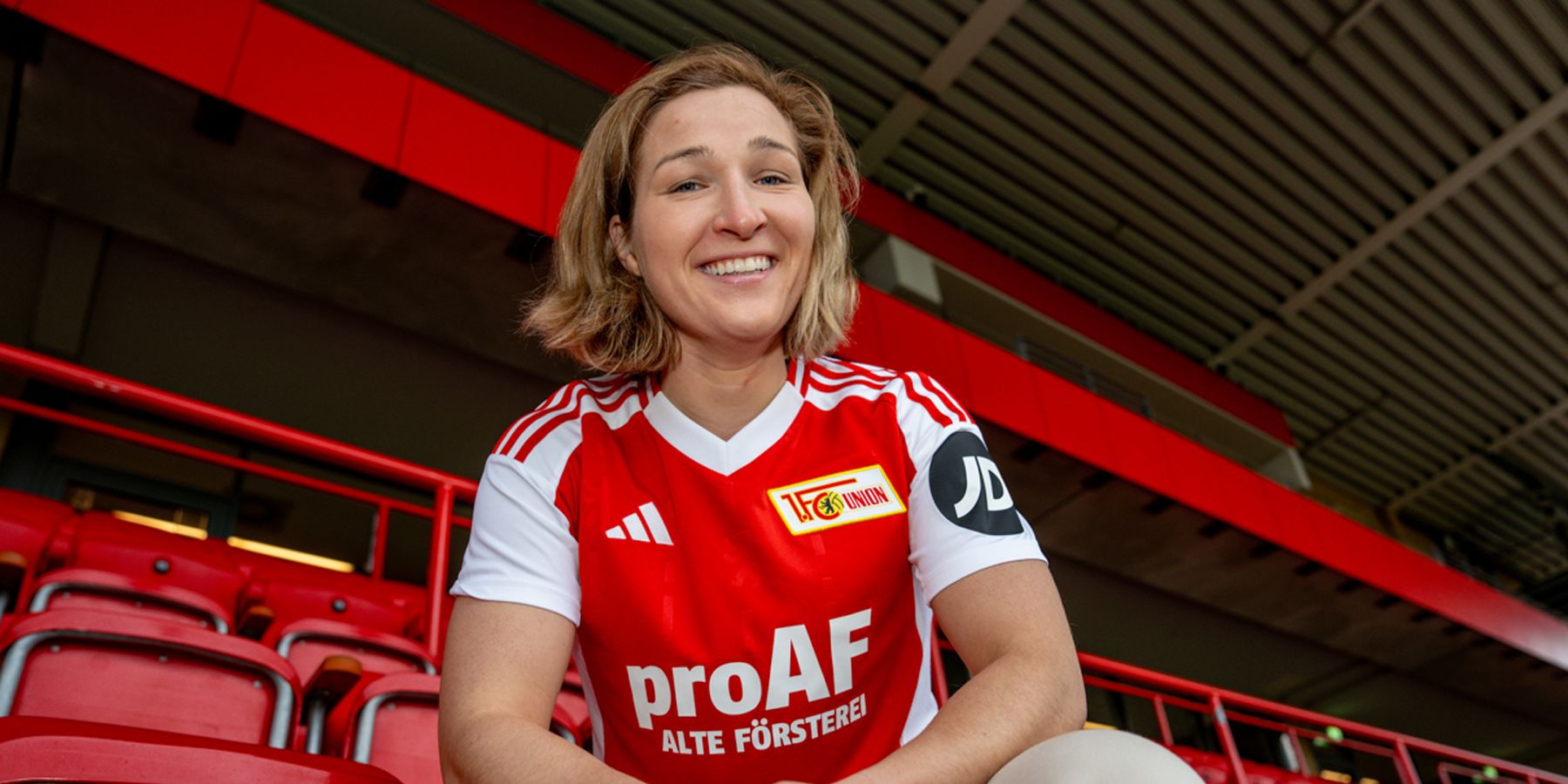 A person in a red soccer jersey is sitting on a chair in a stadium with a red background.