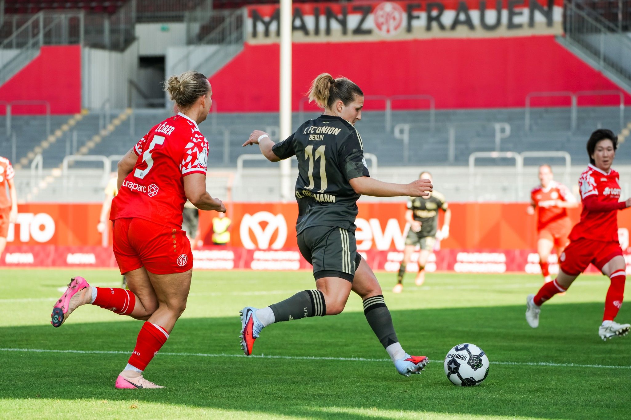 Zwei Fußballspielerinnen im Wettkampf auf dem Spielfeld; eine Spielerin schießt den Ball, während die andere verteidigt.