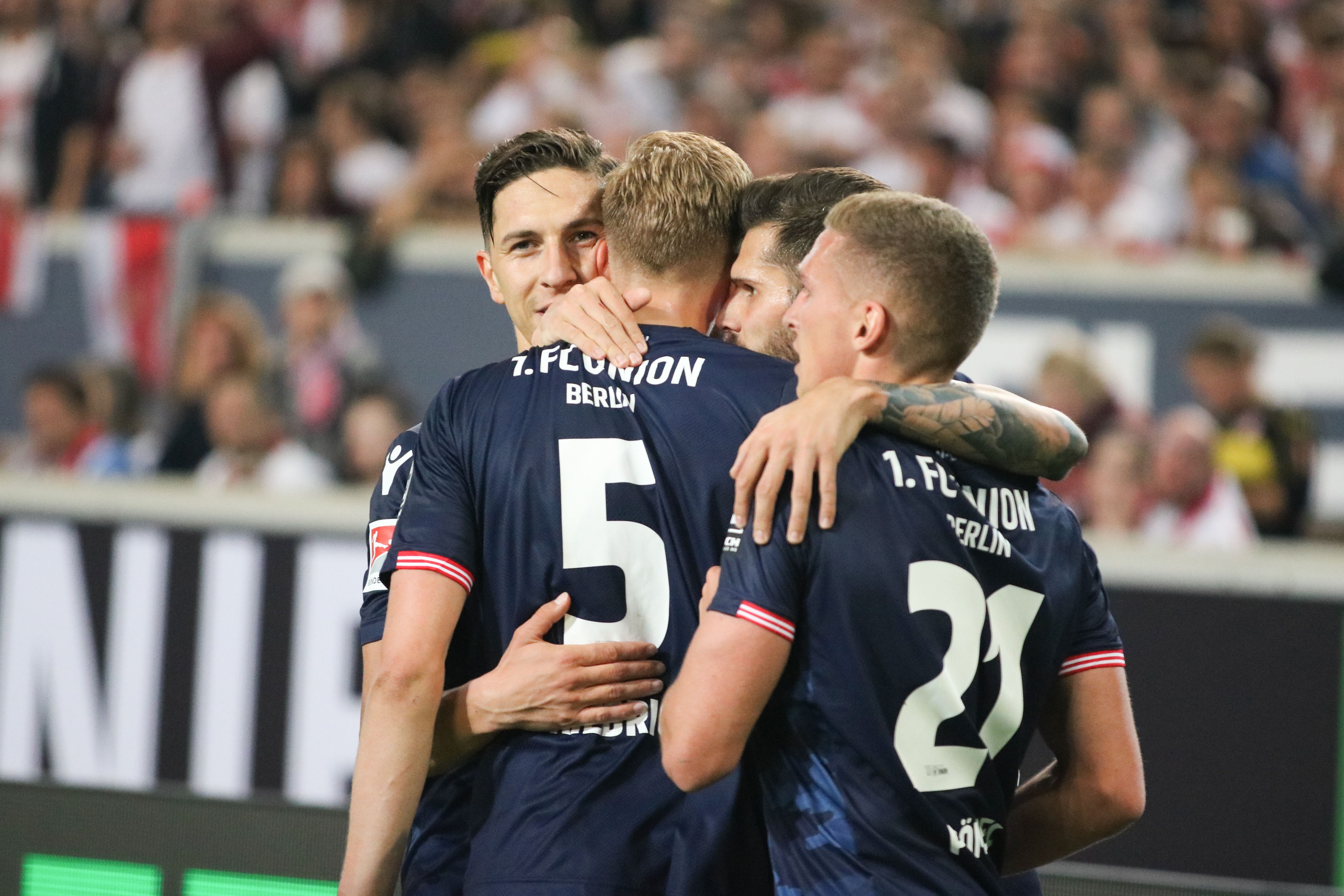 Fußballspieler von 1. FC Union Berlin umarmen sich nach einem Tor, jubelnd und glücklich auf dem Spielfeld.