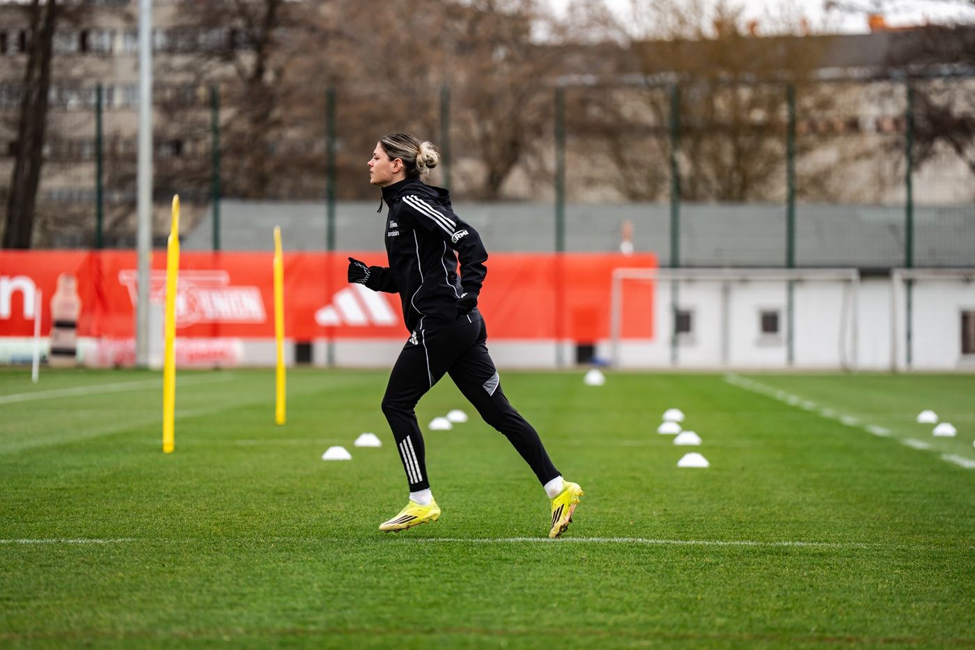 Eine Person in Sportkleidung joggt auf einem Trainingsplatz, umgeben von Markierungshütchen und Toren.