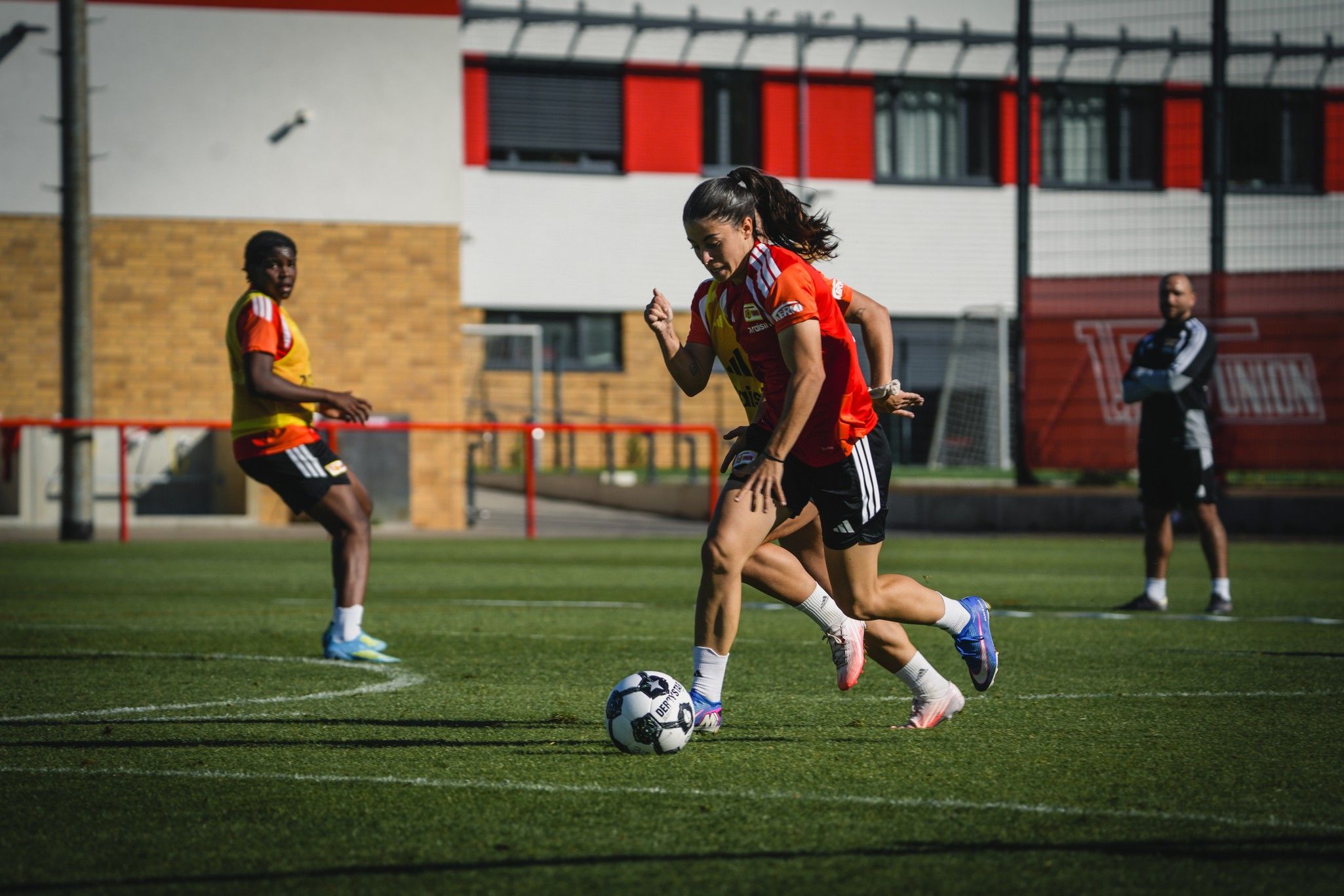 Eine Fußballspielerin dribbelt den Ball während des Trainings, während andere Spieler in der Hintergrund stehen.