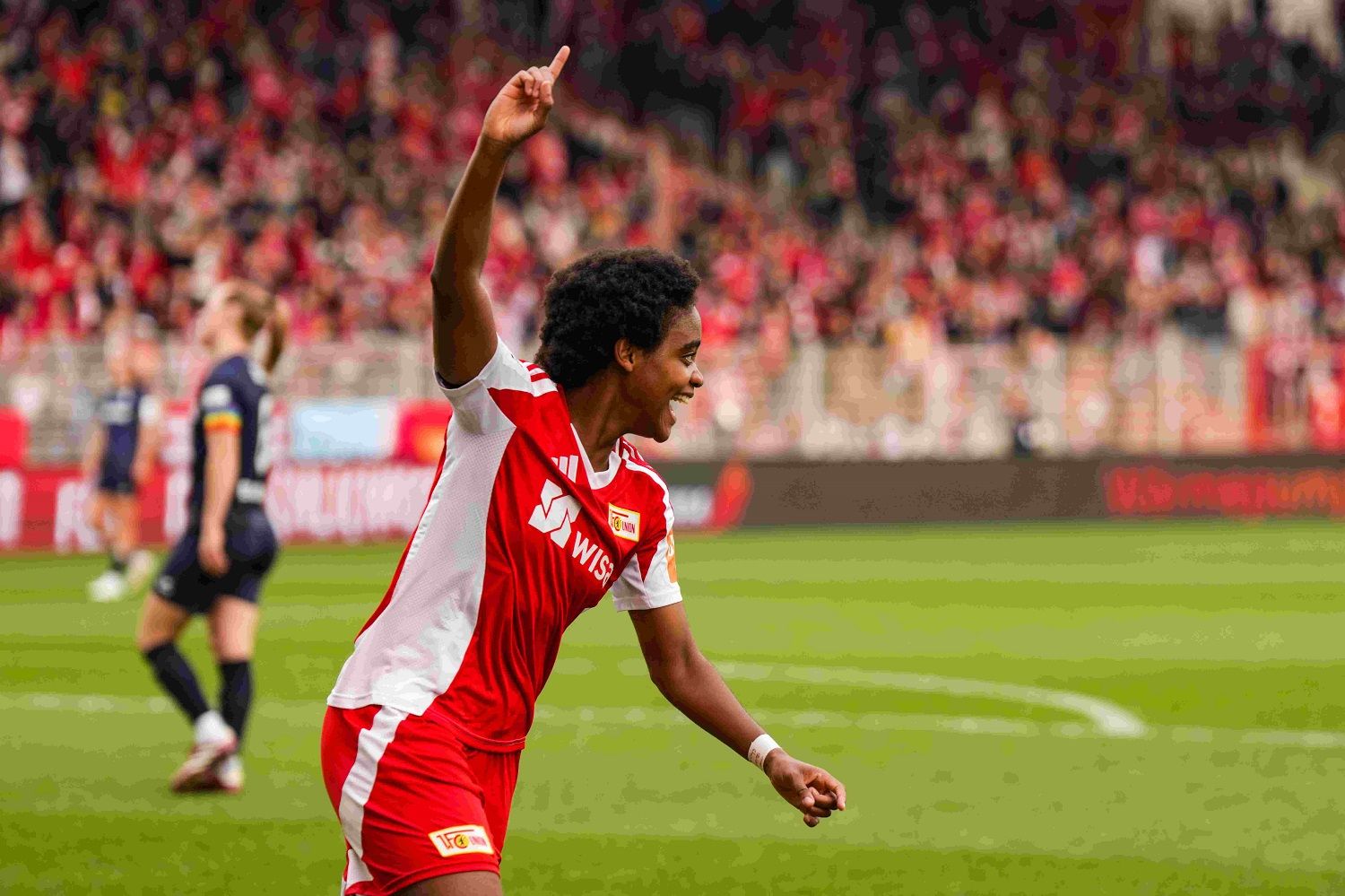 Fußballspieler feiert einen Torerfolg auf dem Platz vor jubelndem Publikum.