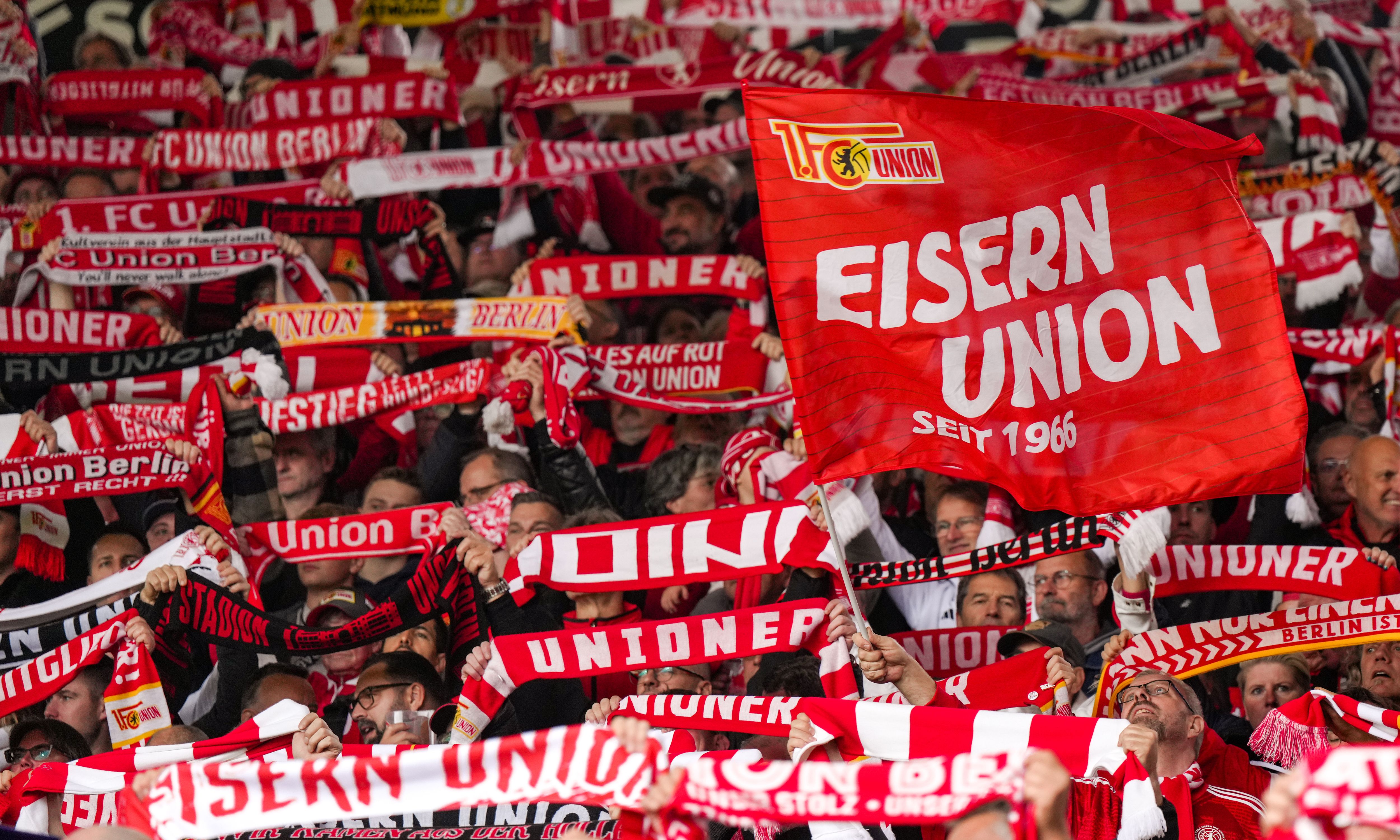 Menschenmenge mit rot-weißen Schals und Fahnen, die die Worte "EISERN UNION" zeigen, in einem Stadion.