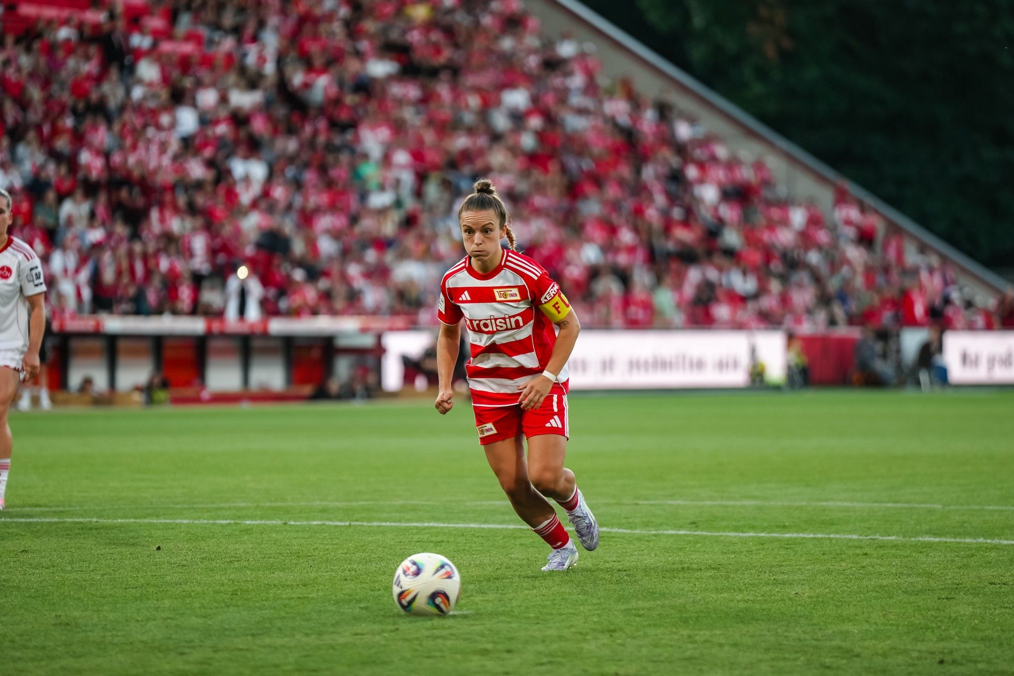 Player in a red striped jersey runs with the ball on a soccer field, with a cheering crowd in the background.