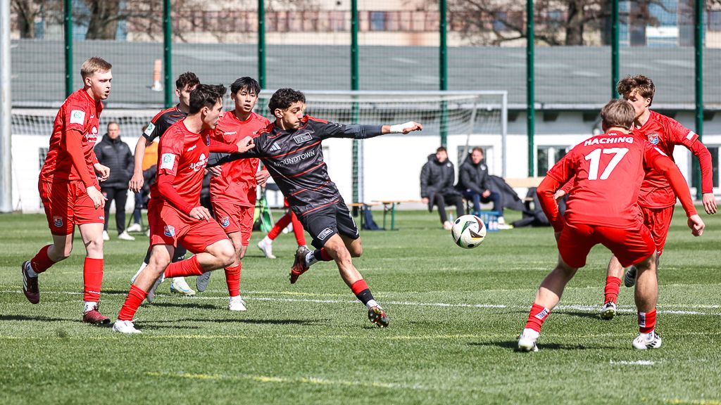Soccer game with players in red and black jerseys fighting for the ball on a green field.