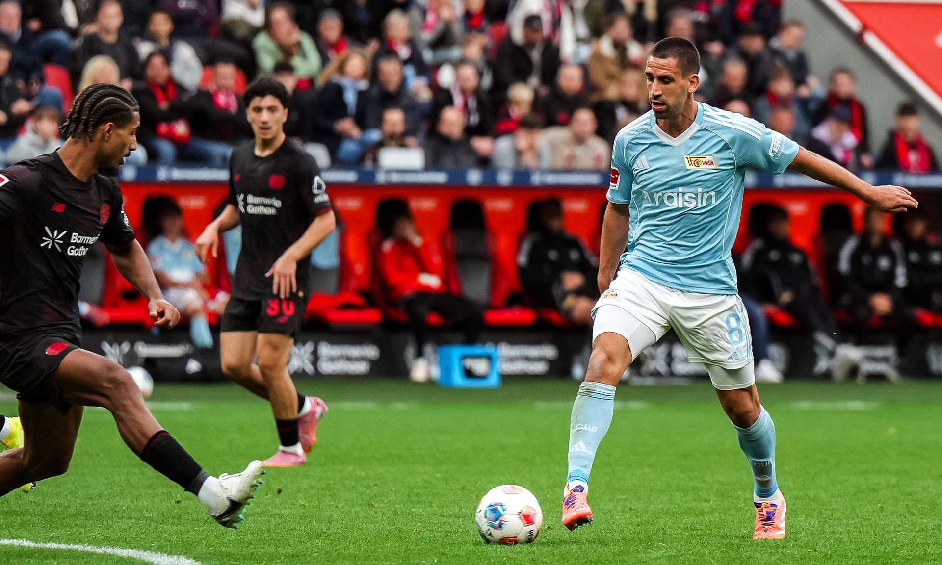 Spielszene eines Fußballs, in der ein Spieler in hellblauem Trikot mit Ball an einem gegnerischen Spieler vorbei dribbelt.