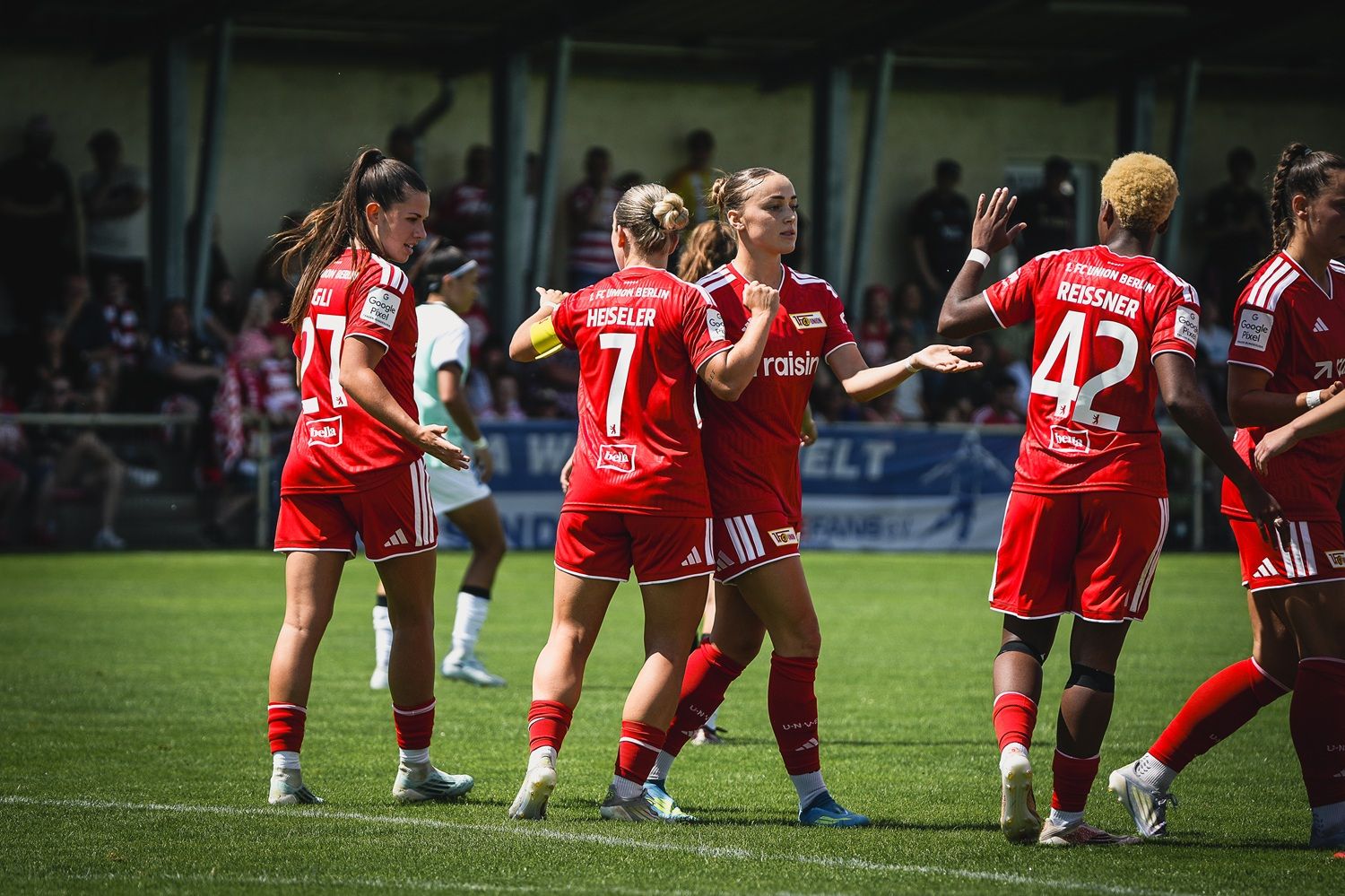 Spielszene einer Frauenfußballmannschaft in roten Trikots, die sich während eines Spiels auf dem Platz unterhält und gestikuliert.