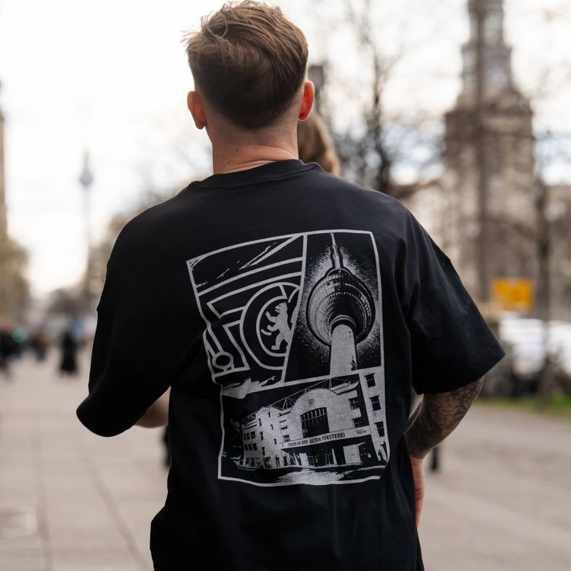 Mann von hinten in einem schwarzen T-Shirt mit grafischem Druck, auf einem urbanen Gehweg in der Stadt.