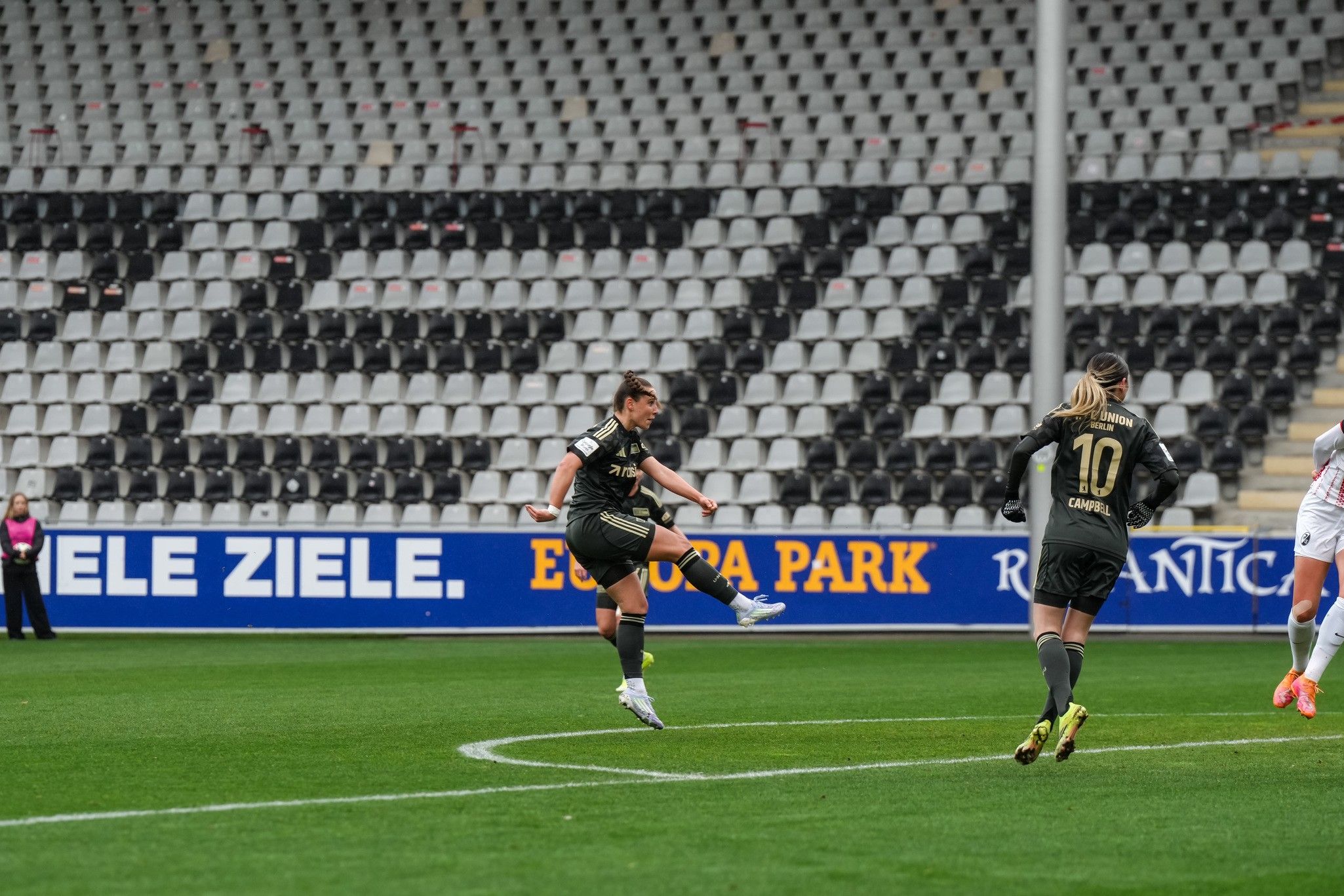 Spielerin schießt den Ball während eines Fußballspiels auf einem leeren Stadionfeld.