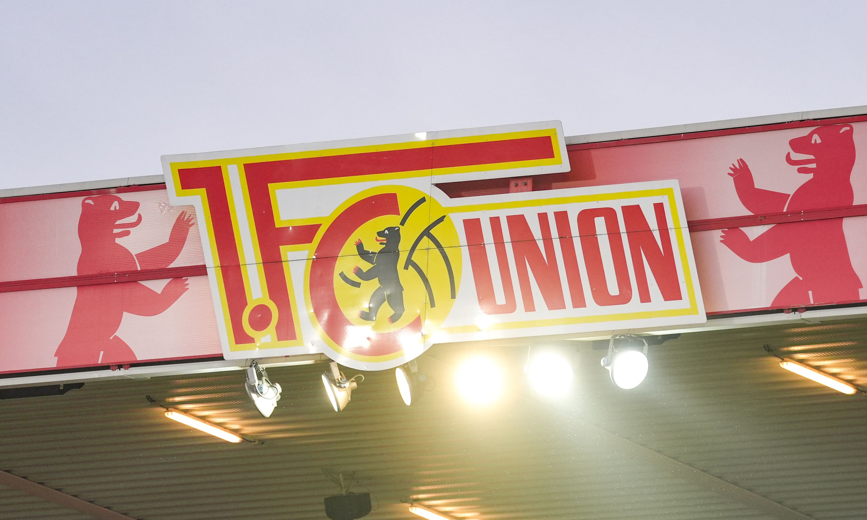 Logo des 1. FC Union Berlin mit zwei roten Bären an den Seiten und Flutlicht im Hintergrund.