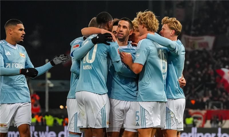 Fünf Fußballspieler in blauen Trikots umarmen sich jubelnd auf dem Spielfeld.