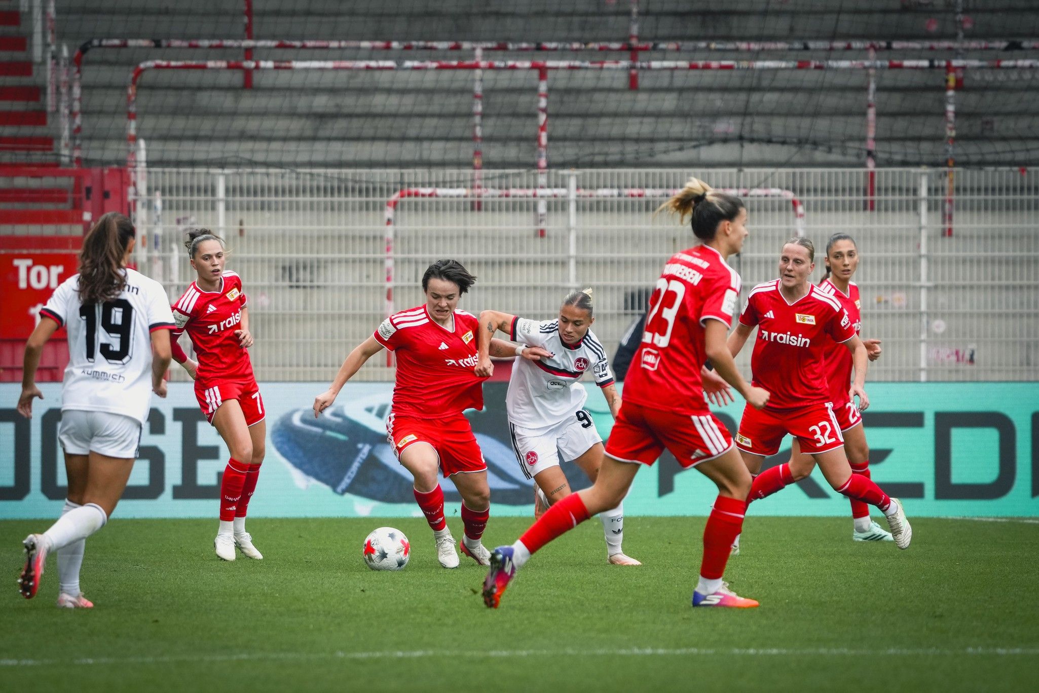 Spielszene eines Frauenfußballspiels, bei dem Spielerinnen in roten und weißen Trikots den Ball im Wettkampf verfolgen.