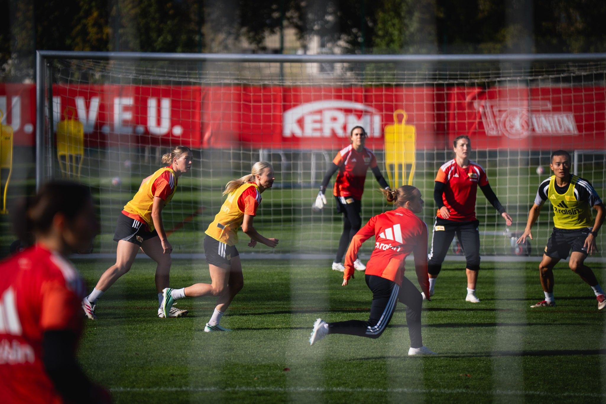 Frauenfußballspielerinnen trainieren auf dem Platz, angeordnet in verschiedenen Positionen, mit einem Tor im Hintergrund.