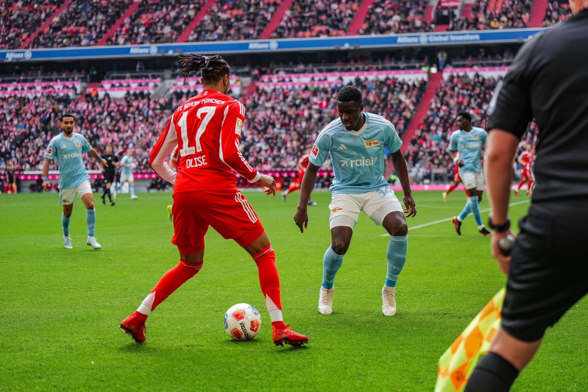 Zwei Fußballspieler, einer in roter und einer in blauer Ausstattung, dribbeln auf einem grünen Spielfeld während eines Spiels.