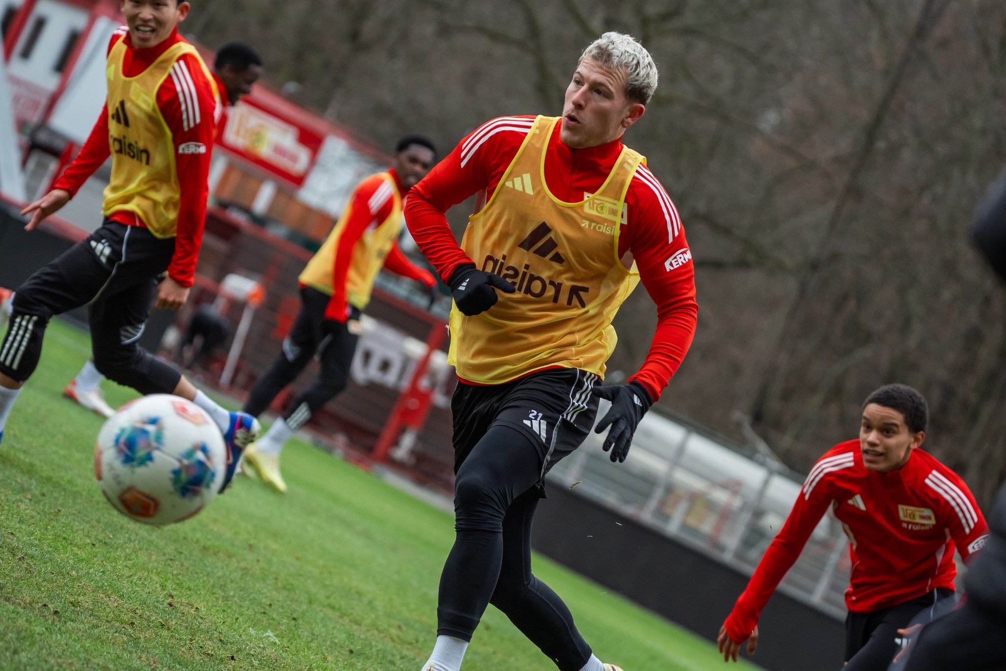 Fußballspieler in roten Trainingsanzügen üben auf einem Rasenplatz, während ein Spieler den Ball rennt.
