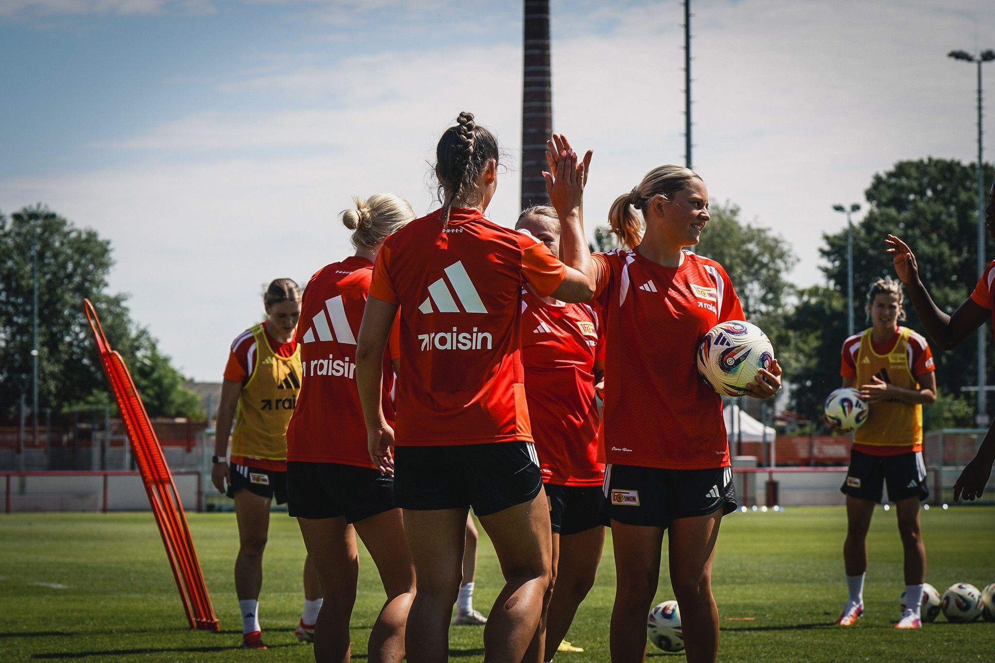 Frauenfußballmannschaft trainiert auf dem Platz, Spielerinnen in roten Trikots mit Bällen und Trainingsmaterialien.