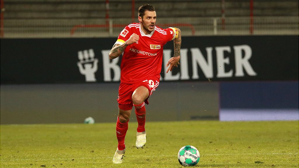Fußballspieler in rotem Trikot sprintet über das Feld, im Hintergrund ist eine Werbetafel sichtbar.