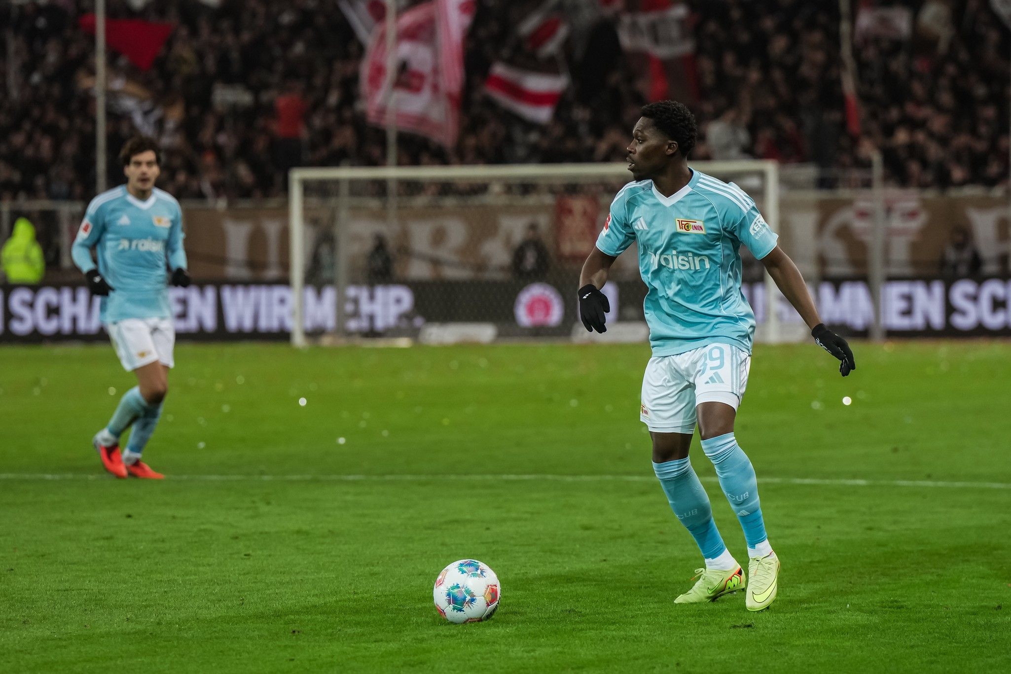 Ein Fußballspieler in hellblauer Ausrüstung steht auf dem Spielfeld und bereitet sich darauf vor, den Ball zu spielen.