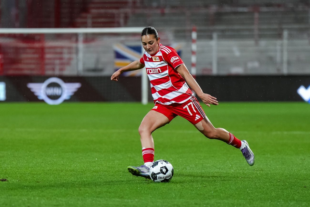 Spielerin in rotem Trikot tritt den Ball auf einem Fußballfeld während eines Spiels.