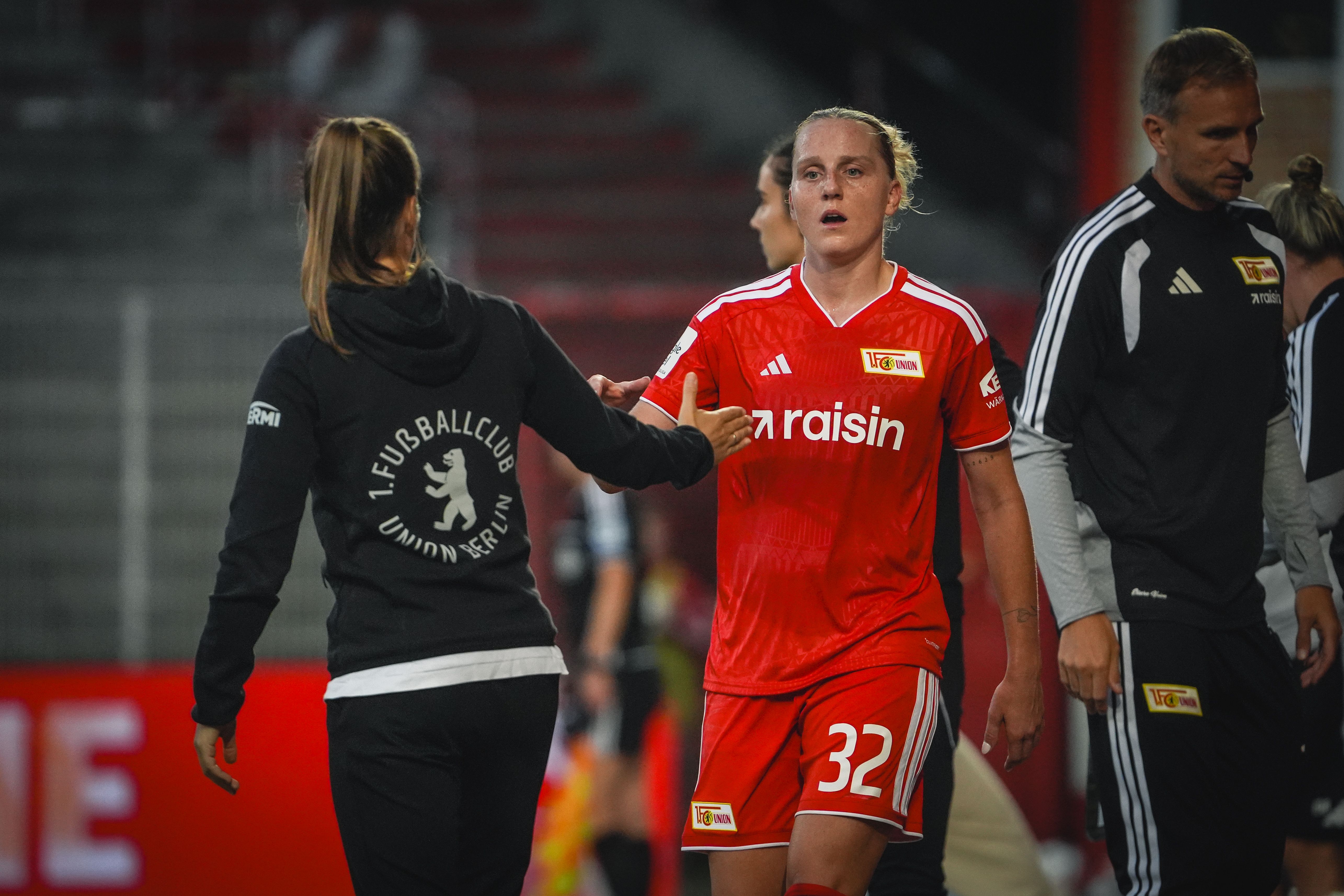 A player in a red jersey with the number 32 is greeted by another person in a black hoodie after a game.