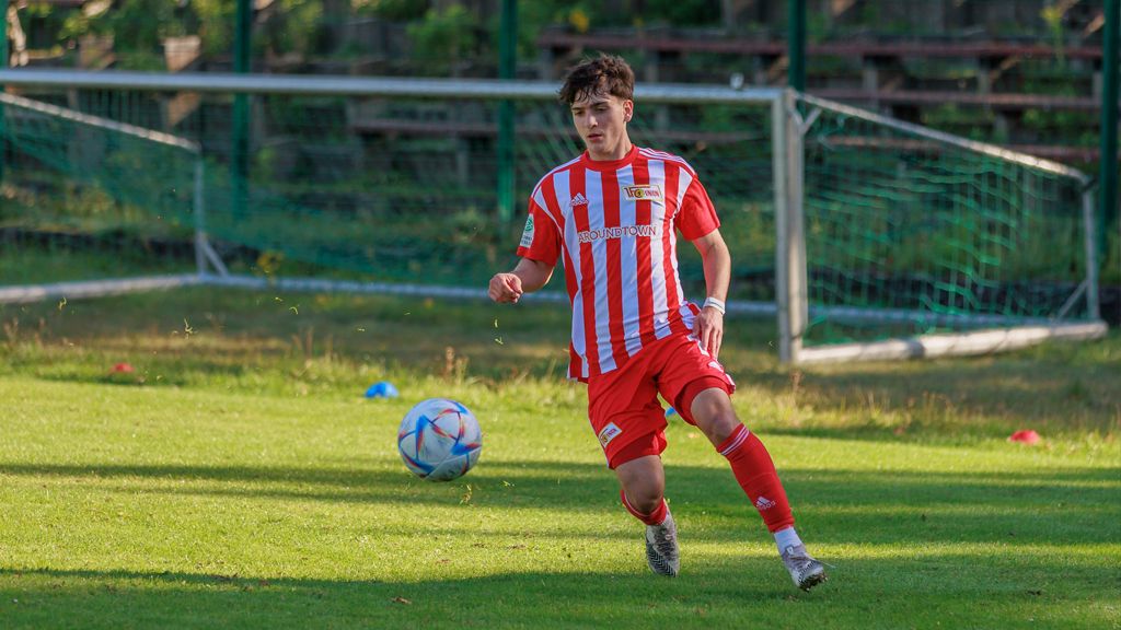 Ein junger Fußballspieler in rot-weißer Uniform läuft über das Spielfeld und bereitet sich auf einen Schuss vor.