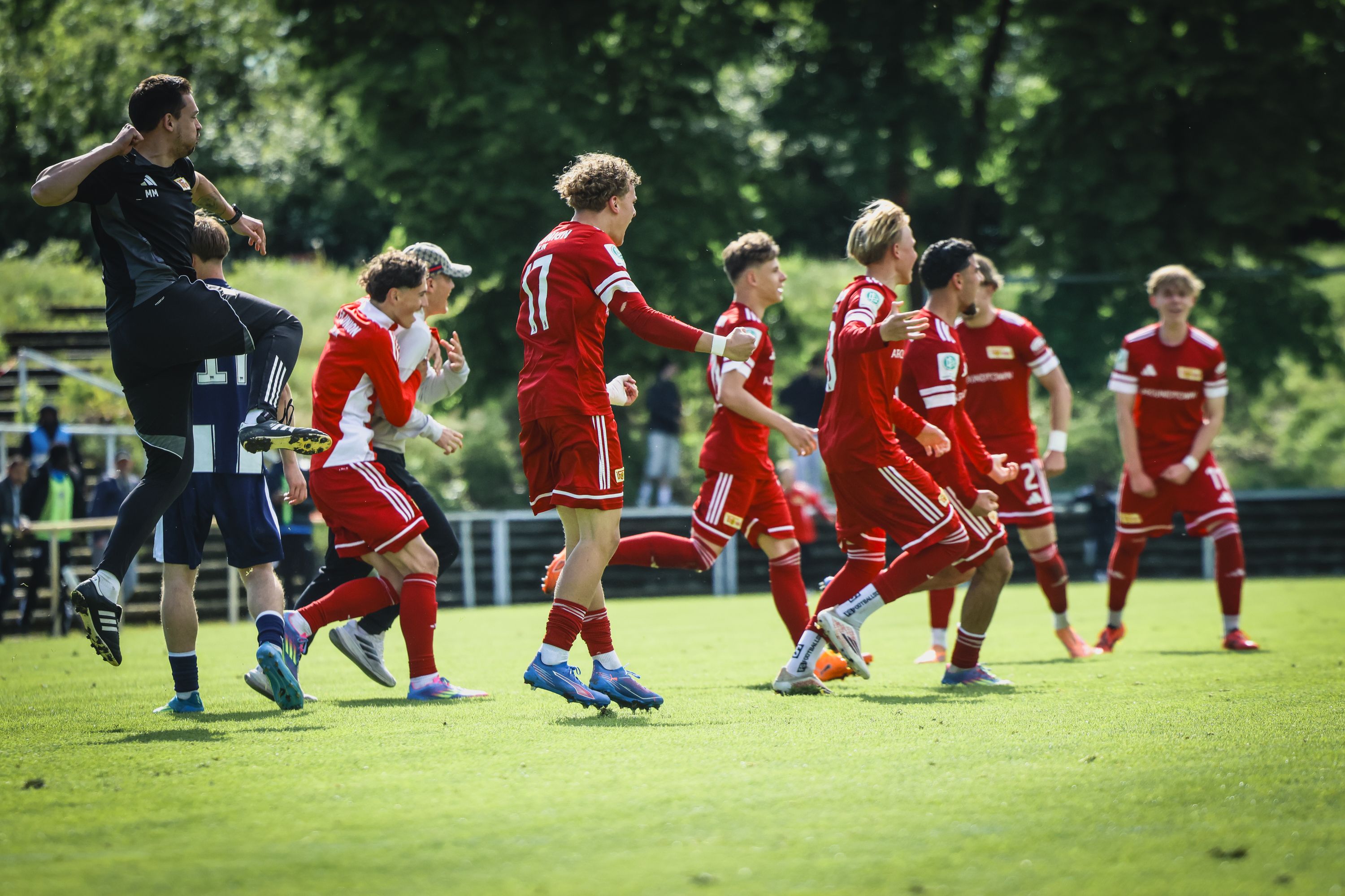 Eine Gruppe von jubelnden Fußballspielern in roten Trikots feiert einen Torerfolg auf einem grünen Spielfeld.