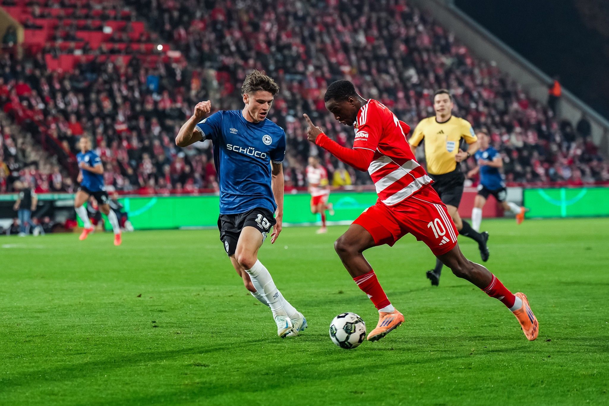 Zwei Fußballspieler kämpfen um den Ball auf einem Rasenplatz während eines Spiels.