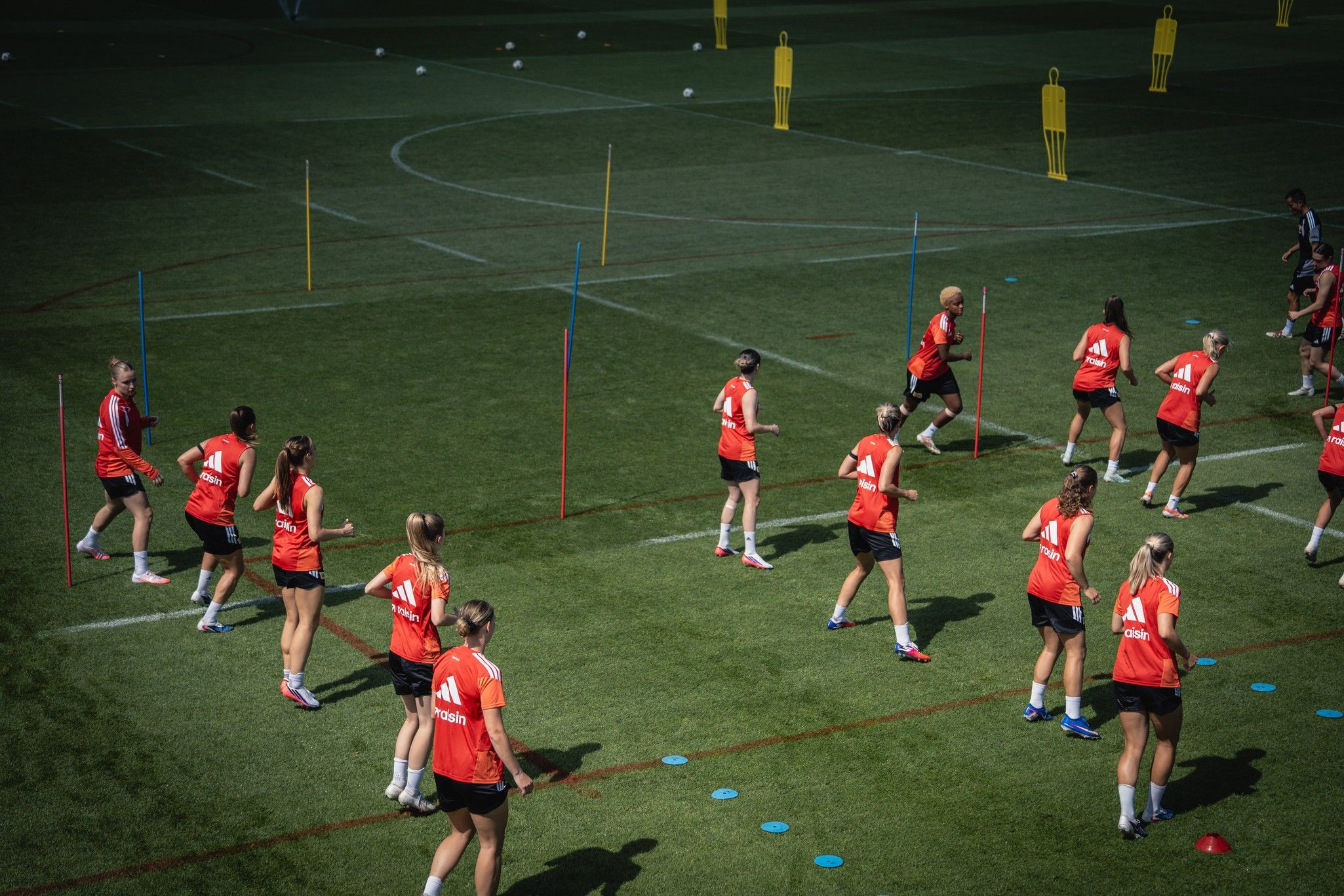Mannschaftstraining auf einem Fußballfeld mit spielenden Frauen in roten Trikots und verschiedenen Trainingshilfen.
