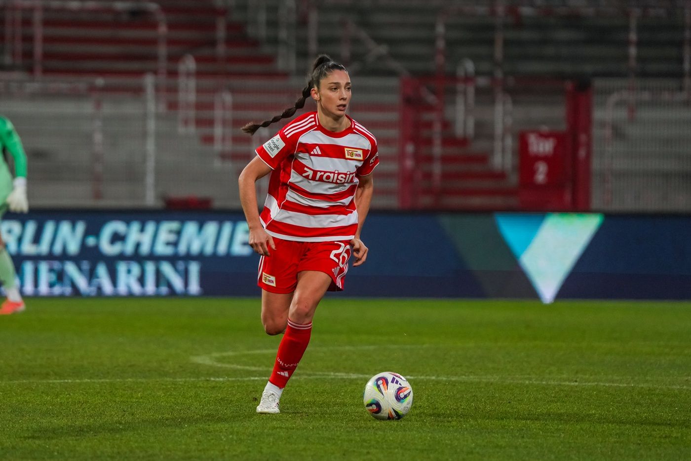 Eine Fußballspielerin in rot-weißer Uniform läuft mit dem Ball auf dem Spielfeld.