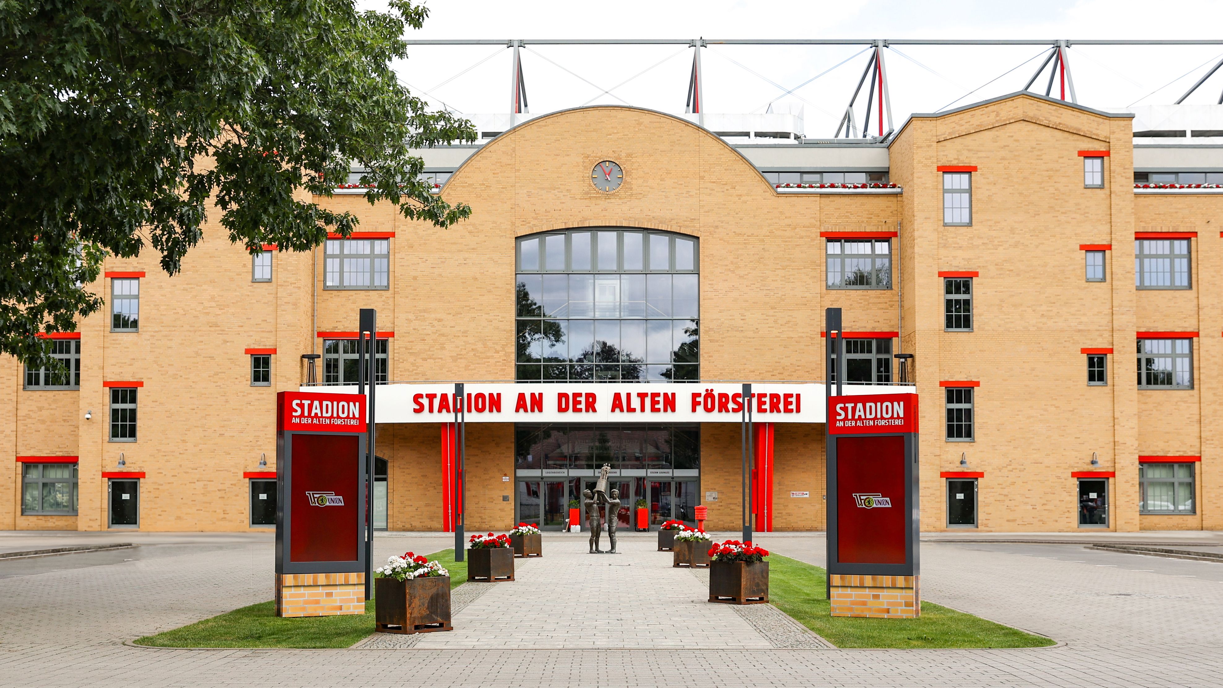Eingang zum Stadion an der Alten Försterei mit rot-weißen Akzenten und Blumenarrangements im Vordergrund.