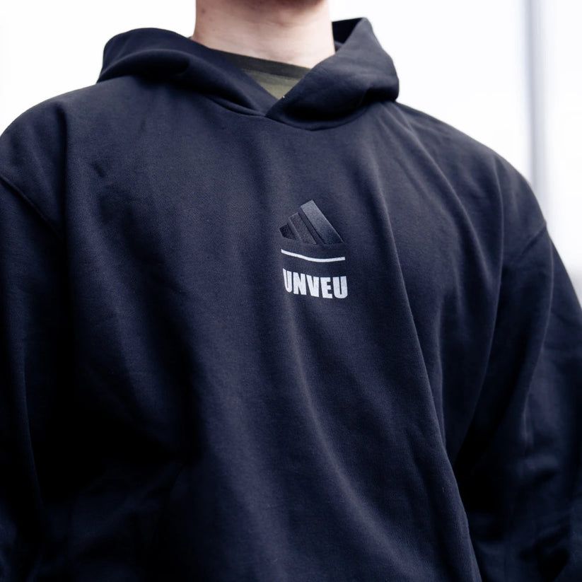 Mann trägt einen schwarzen Hoodie mit dem Logo "UNVEU" und einem Adidas-Symbol.