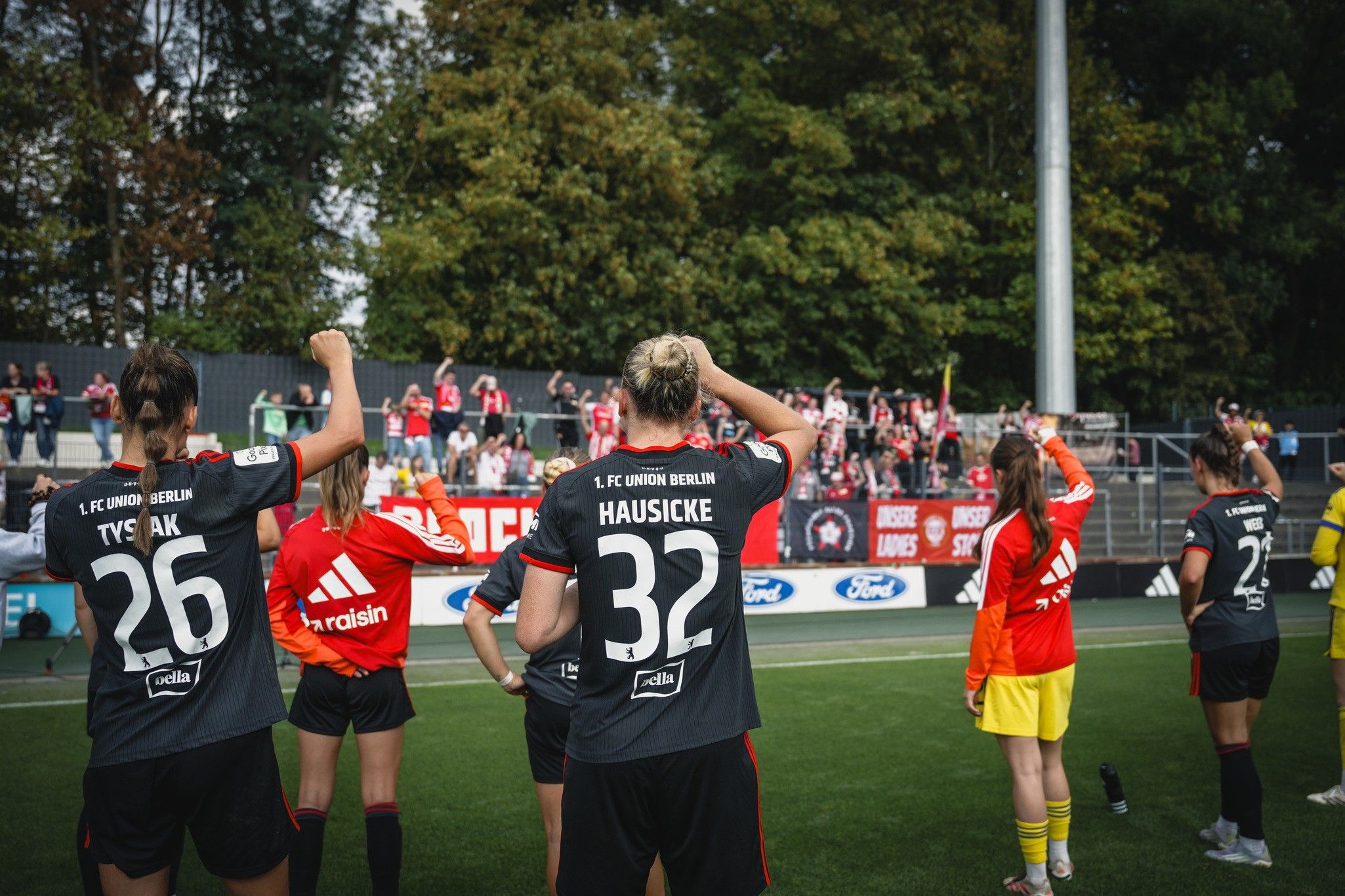 Spielerinnen des 1. FC Union Berlin in schwarzer Spielkleidung stehen beim Spiel, im Hintergrund jubelnde Fans.