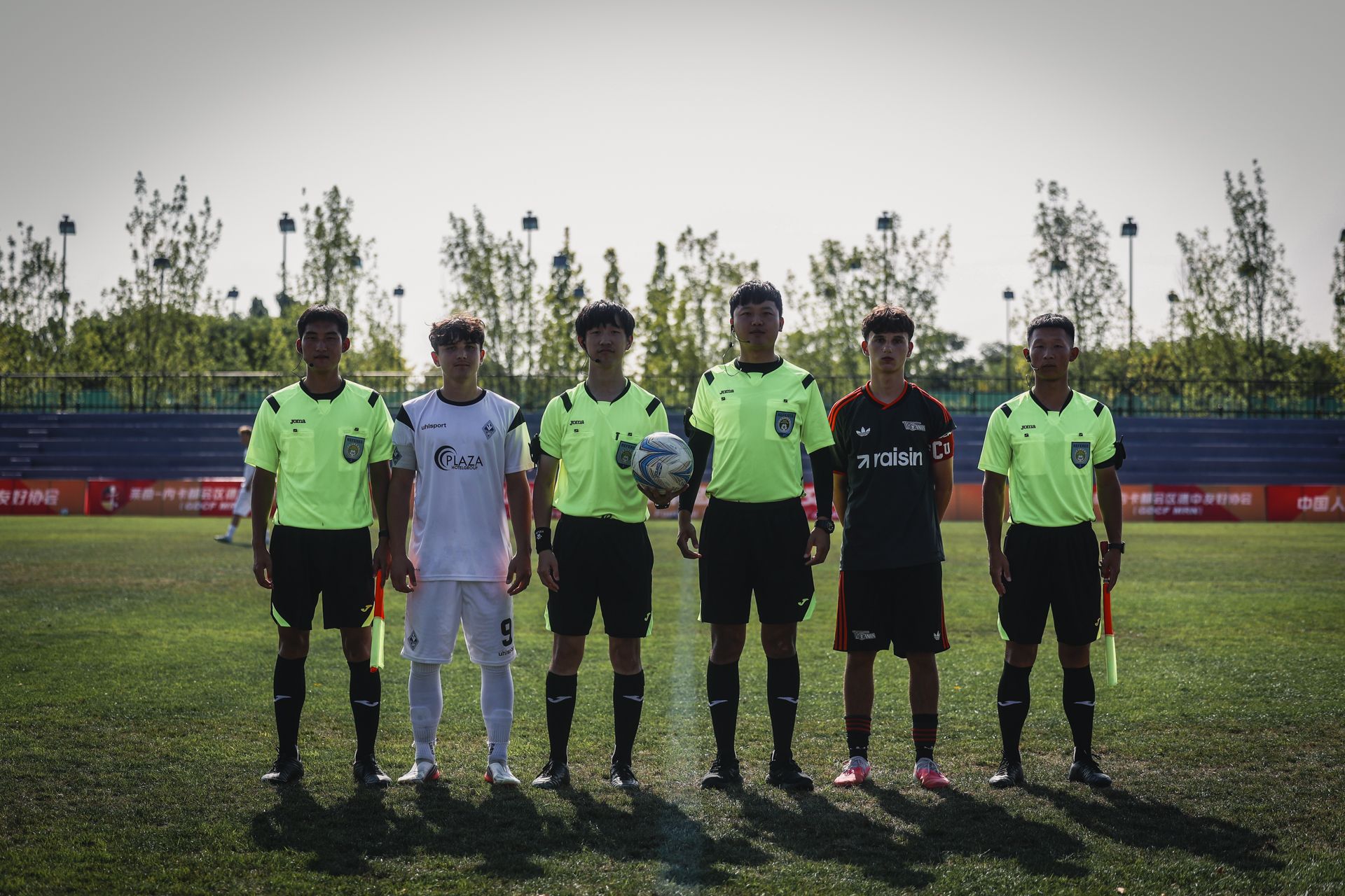 Sechs Fußballspieler und Schiedsrichter in leuchtend grünen Trikots posieren auf einem Spielfeld vor einem Spiel.