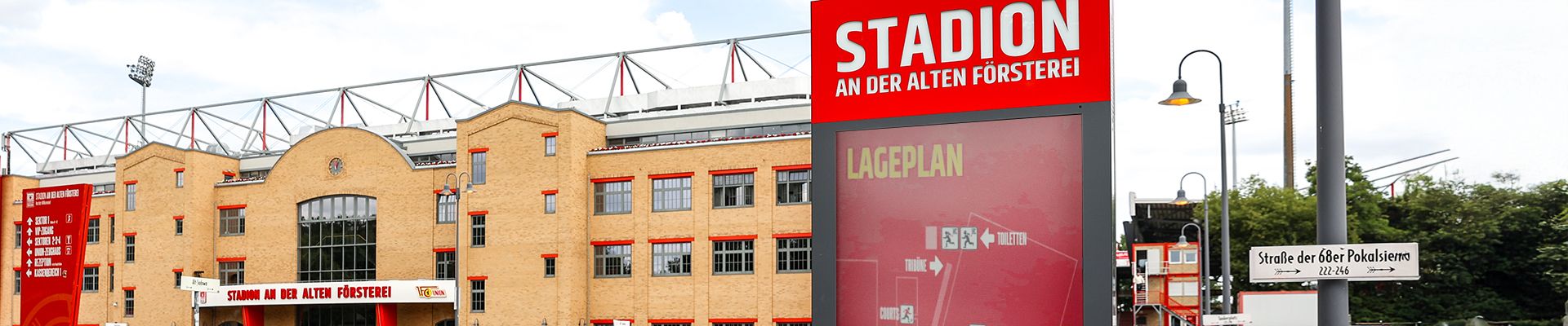 Ein Stadiongebäude mit roter Beschilderung und einem Wegweiser in der Nähe, umgeben von einem grünen Bereich.