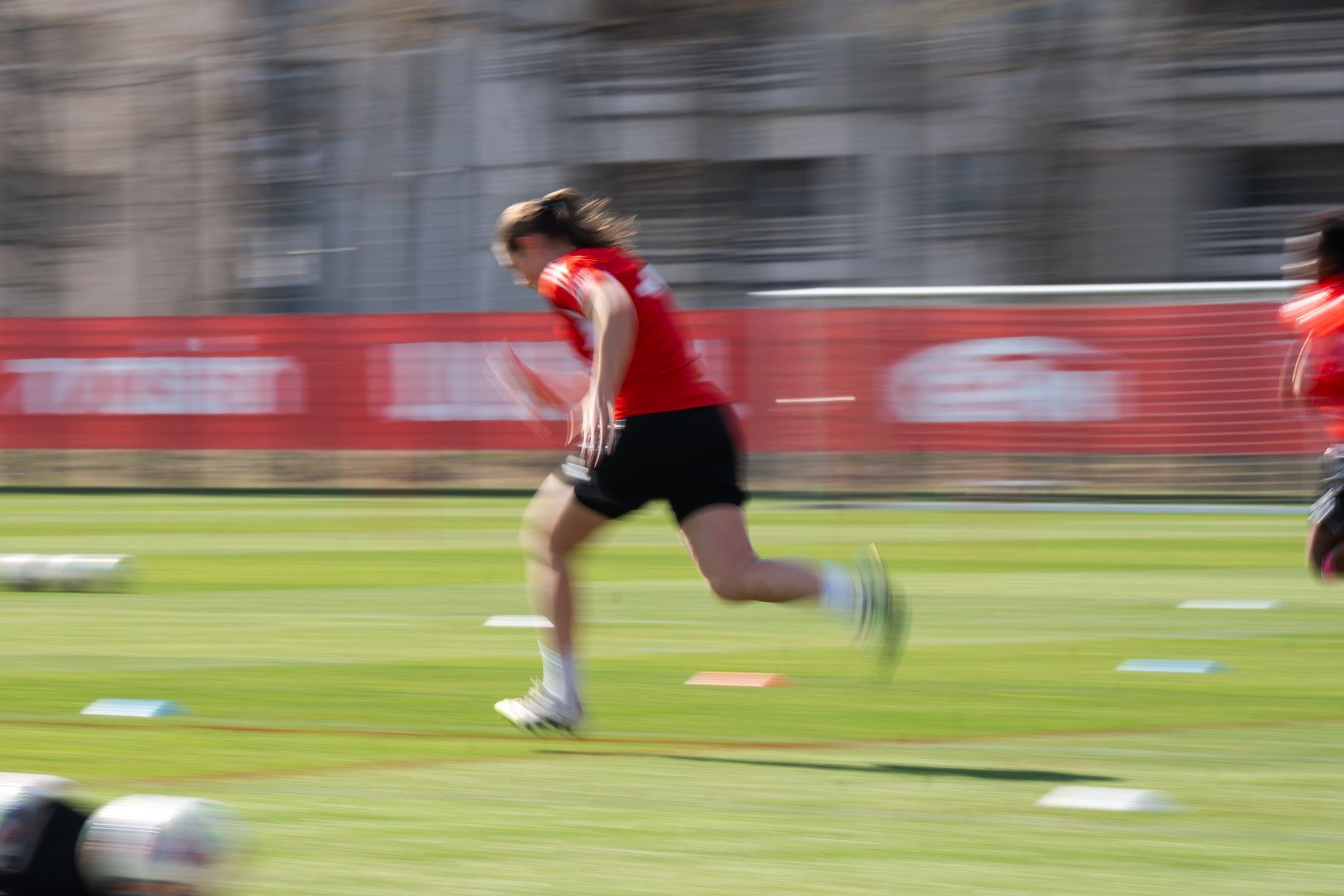 Eine Person in rotem Trikot sprintet über einen grünen Sportplatz, der Hintergrund ist verschwommen.
