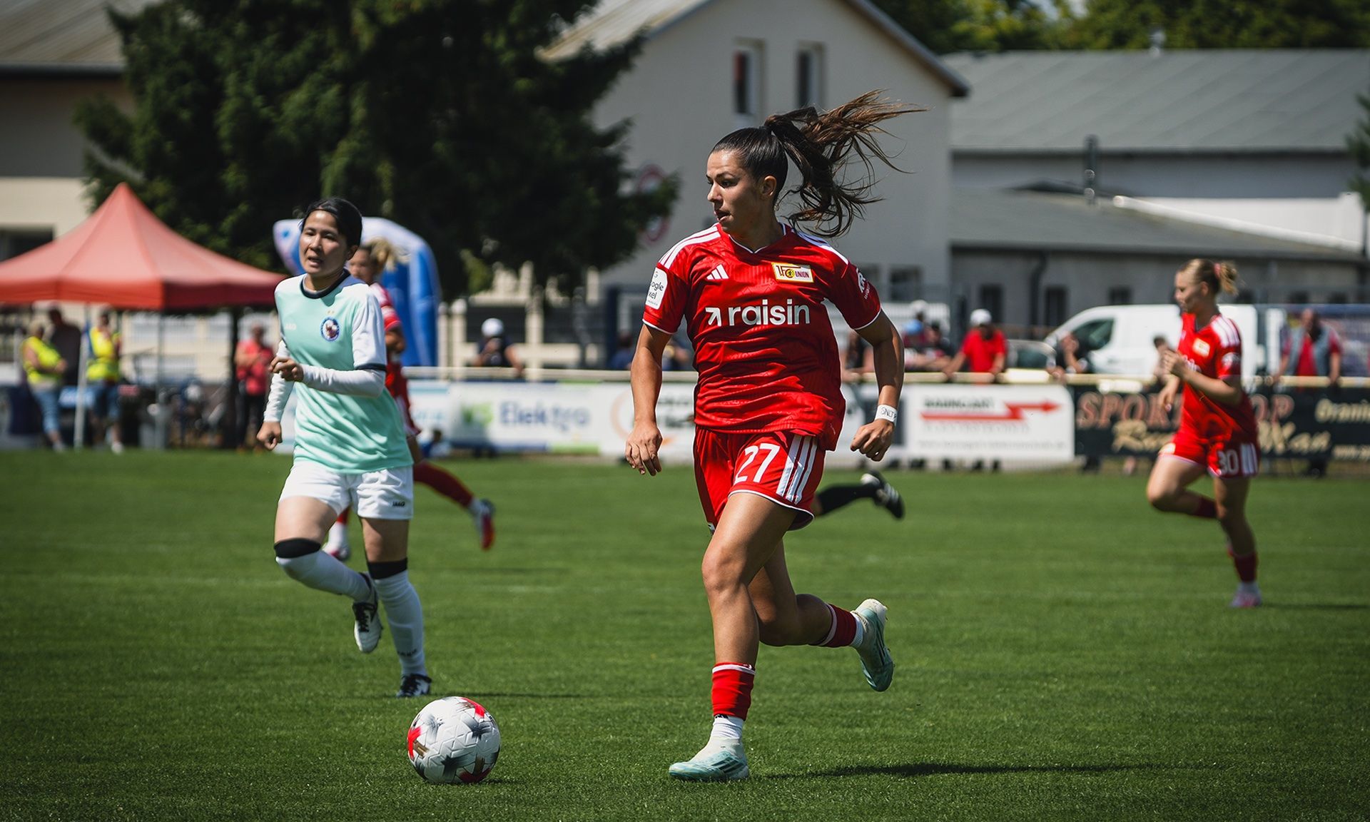 Eine Fußballspielerin der Mannschaft Union Berlin trägt ein rotes Trikot und dribbelt den Ball auf einem Spielfeld.