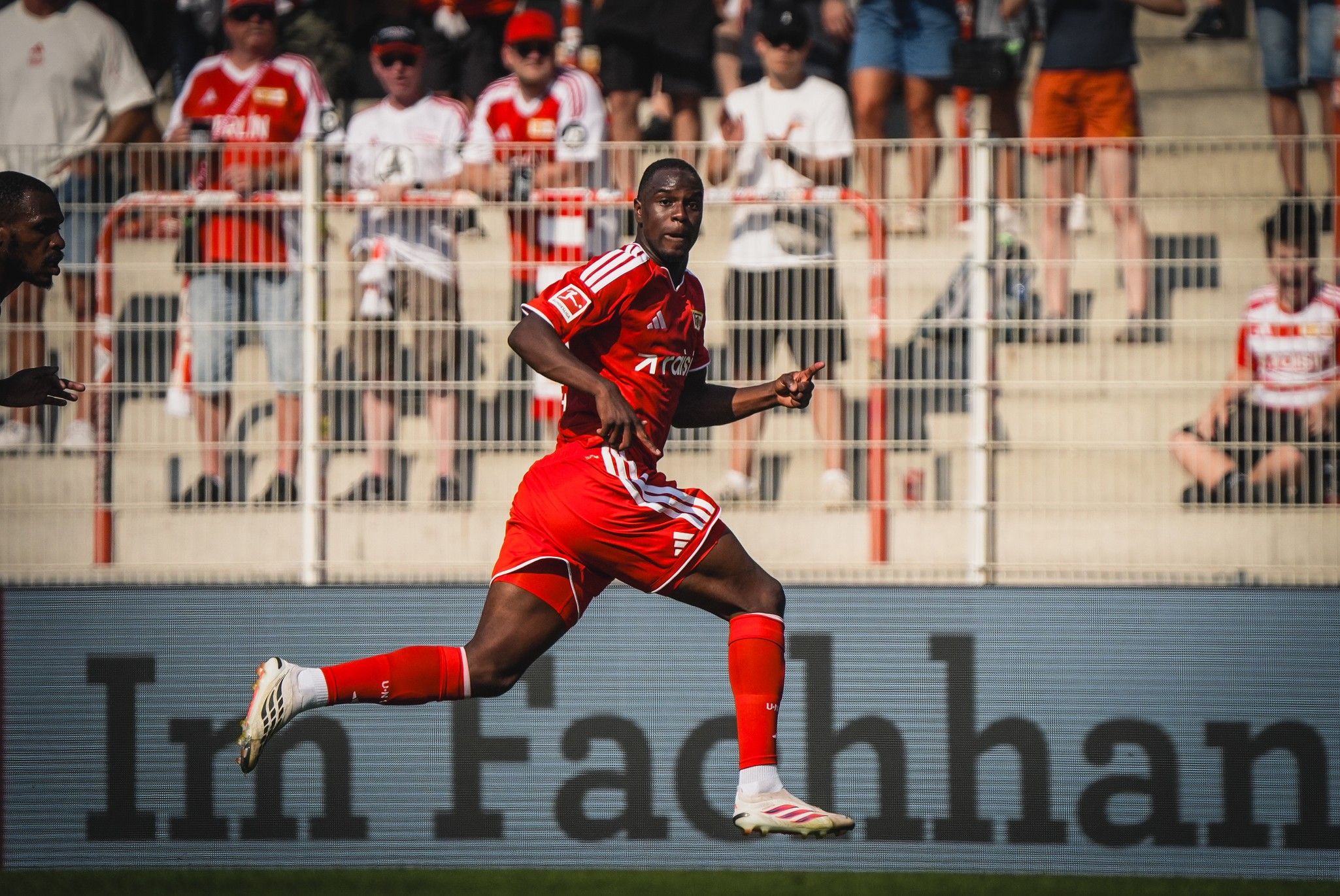 Ein Fußballspieler in rotem Trikot sprintet auf dem Platz, im Hintergrund eine jubelnde Menschenmenge.