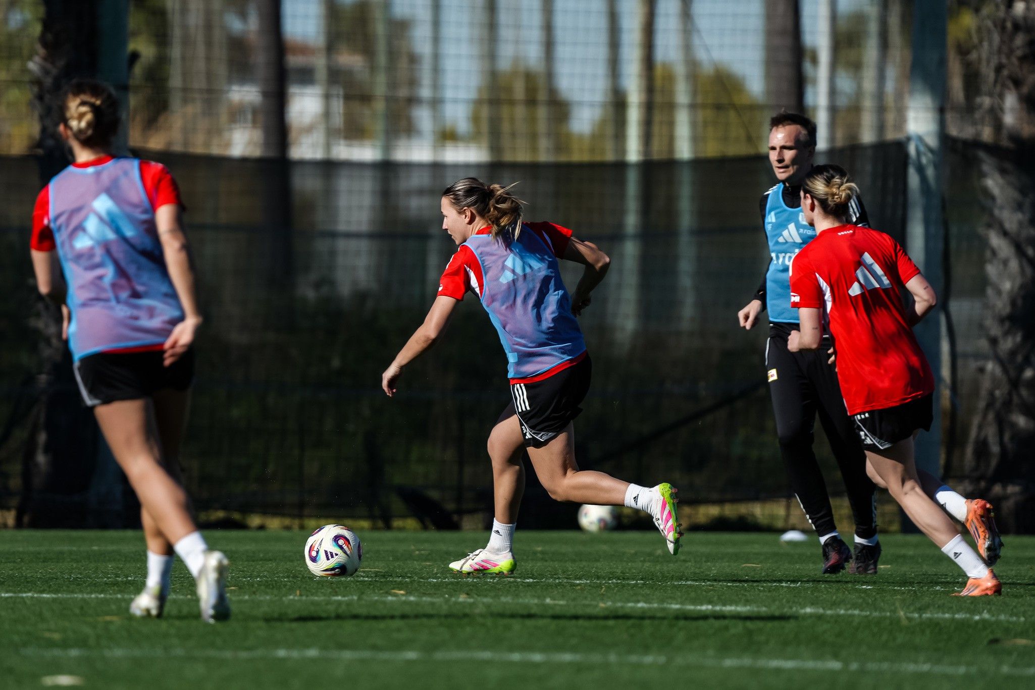 Spielerinnen trainieren auf dem Fußballplatz, während sie den Ball dribbeln und sich in Richtung Tor bewegen.