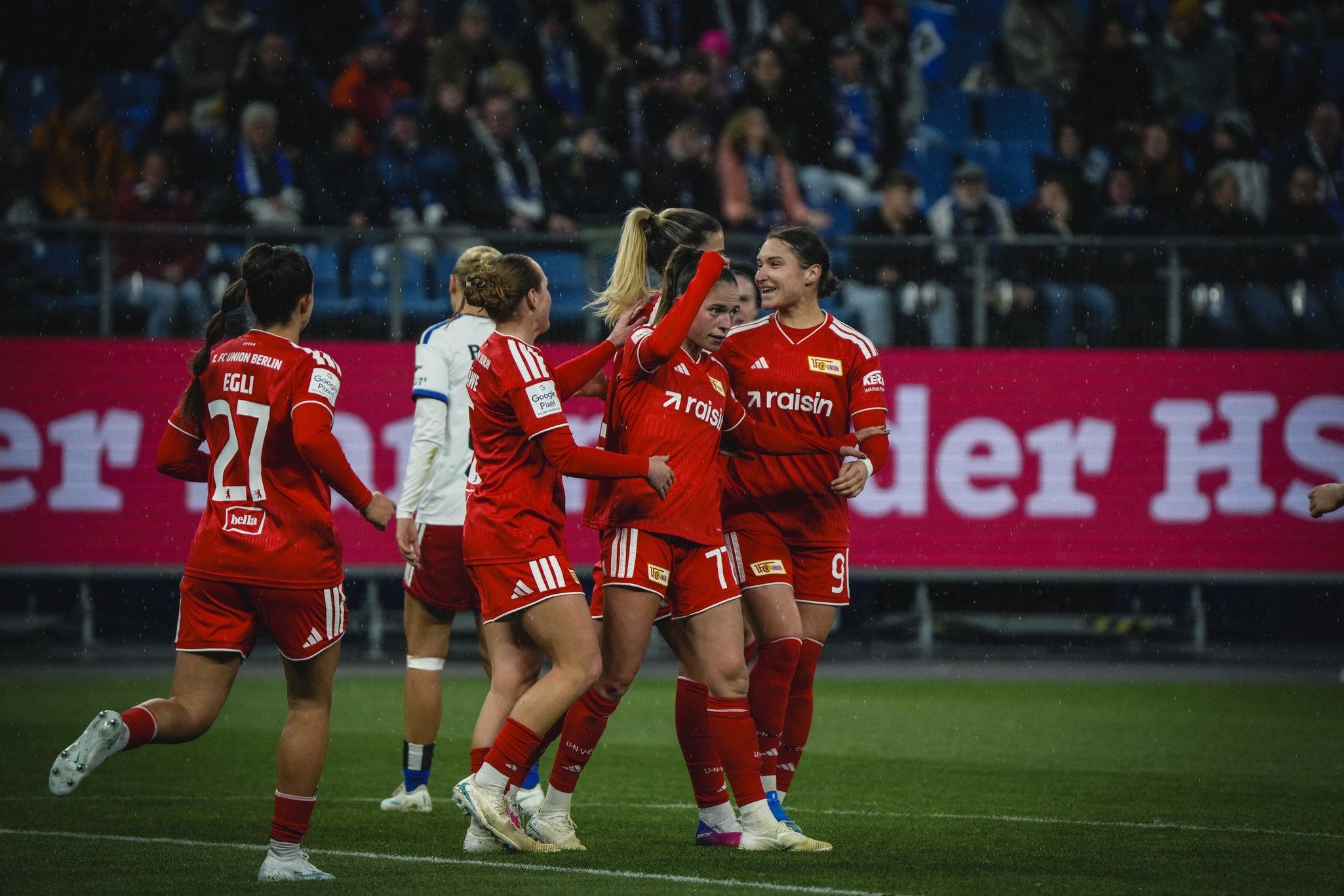 Spielerinnen des FC Union Berlin feiern einen Treffer in einem Fußballspiel, umgeben von jubelnden Fans.