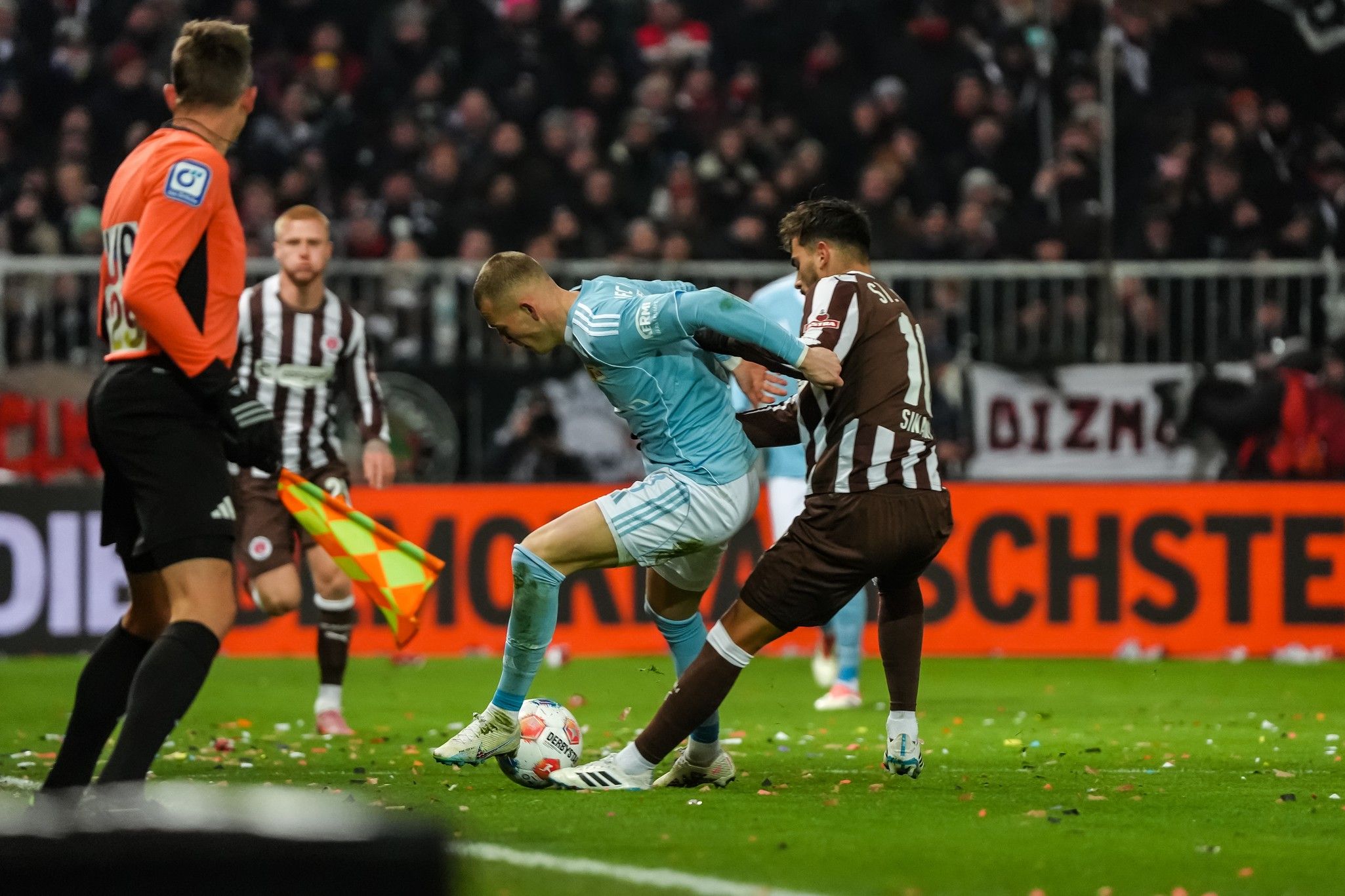 Zwei Fußballspieler im Wettkampf um den Ball, mit Zuschauern im Hintergrund, in einem Stadion bei einer Sportveranstaltung.