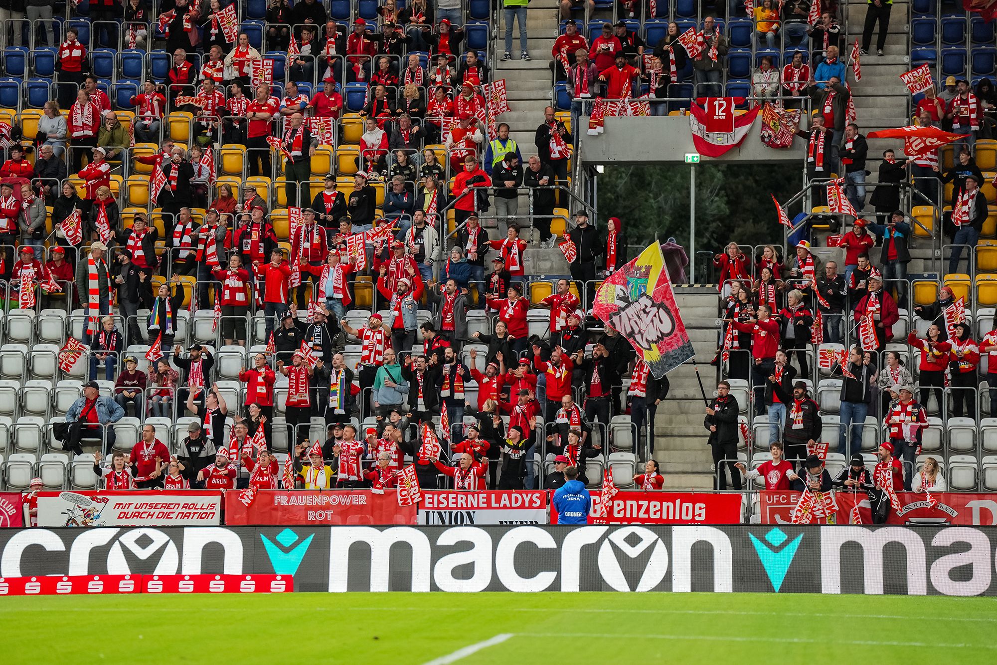 Eine begeisterte Fangemeinde in roter Kleidung, die Fahnen schwenkt und Schals hält, steht im Stadion.
