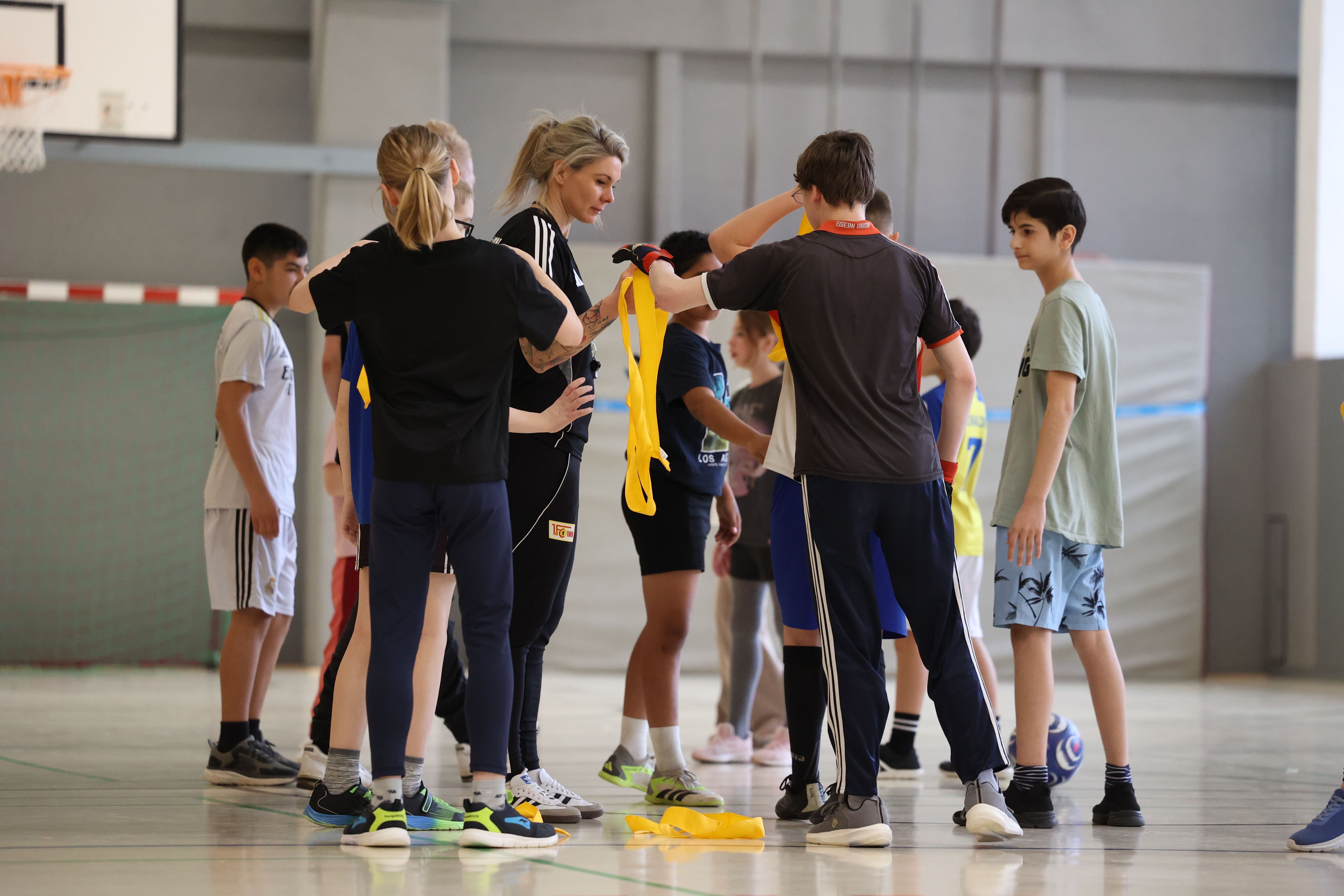 Eine Gruppe von Kindern und Jugendlichen im Sport, die mit einem Trainer gelbe Westen anprobieren.