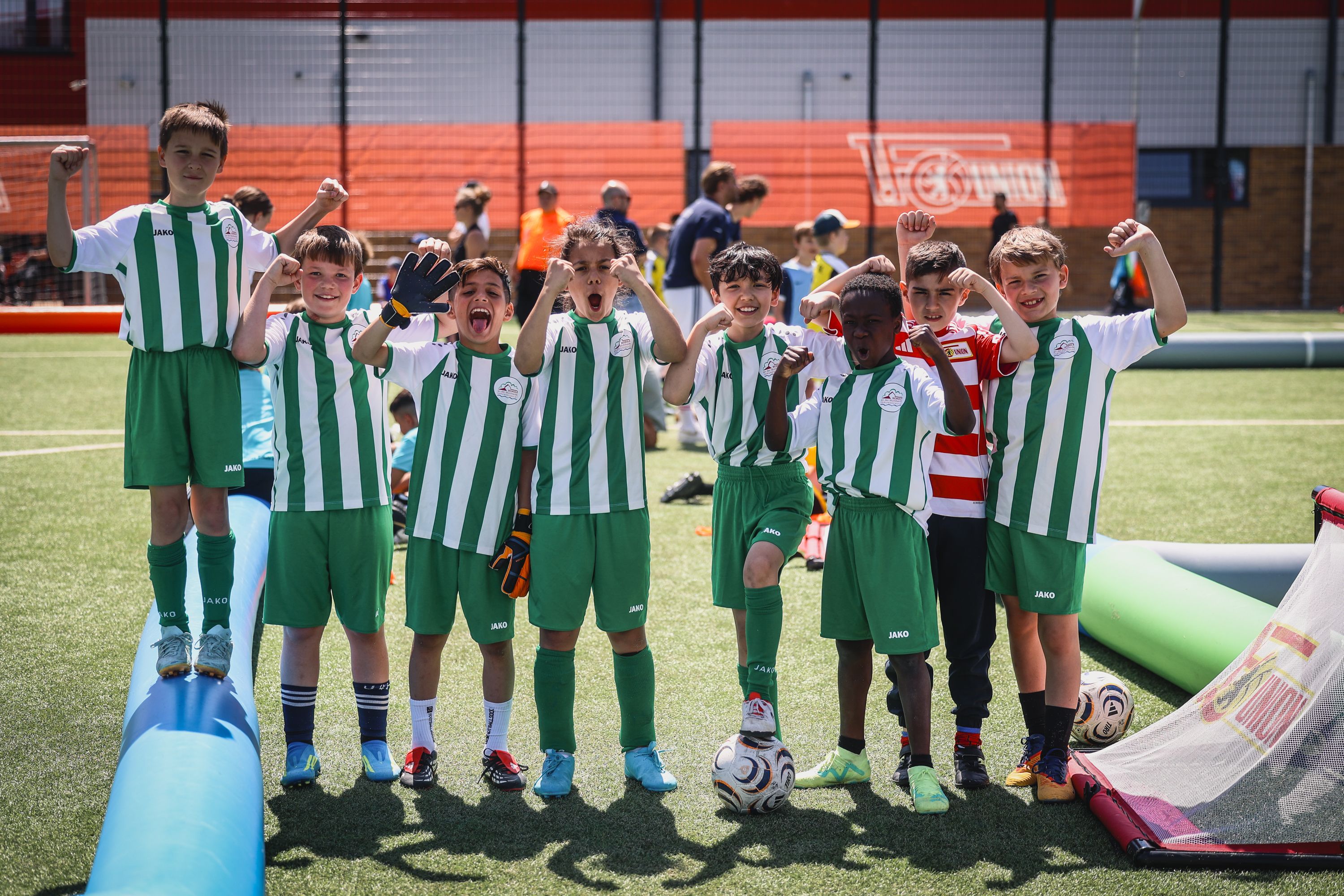 Eine Gruppe von acht Jungen in grünen Fußballtrikots steht auf einem Spielfeld und posiert jubelnd.