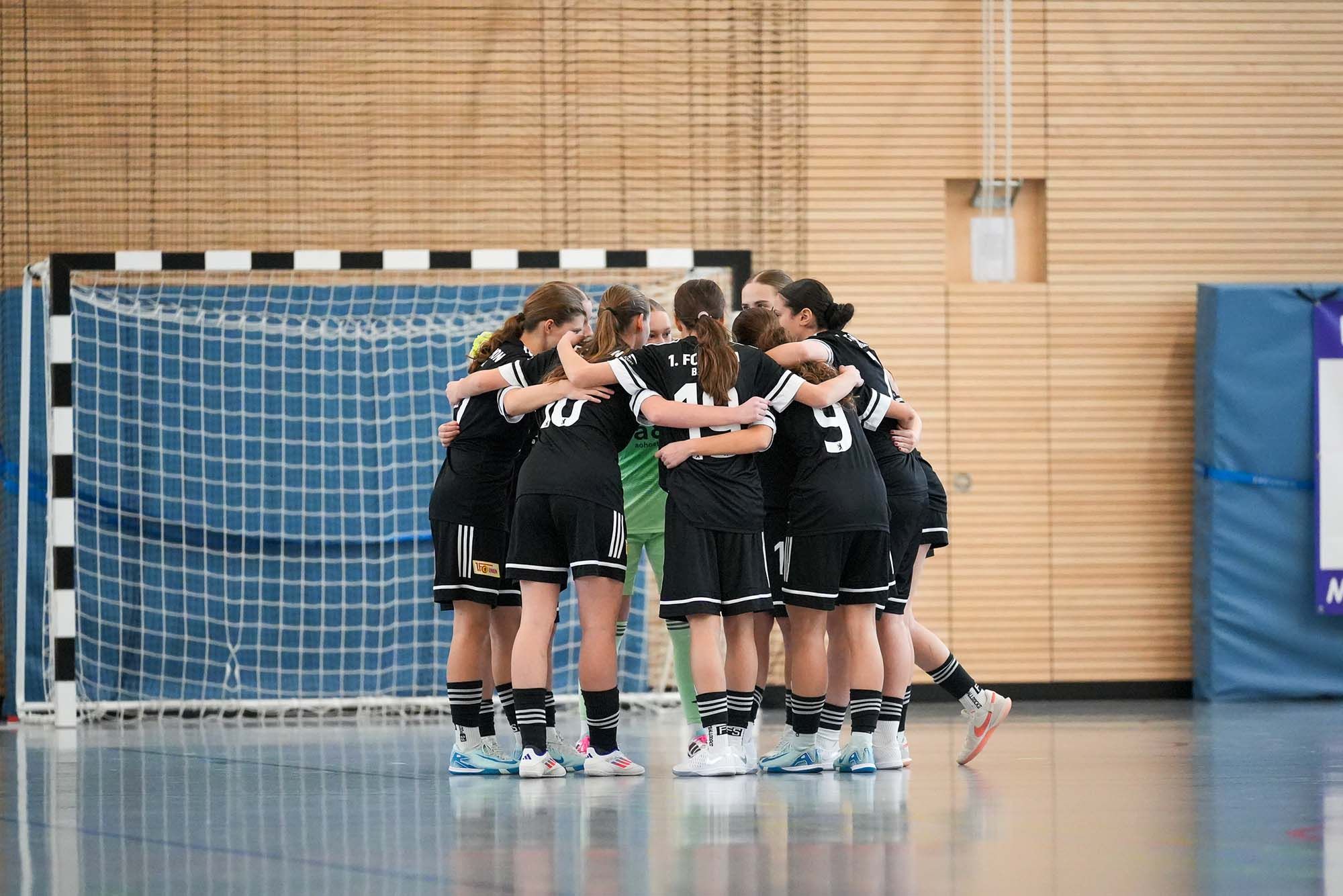 Eine Gruppe von Fußballspielerinnen steht in einem Huddle auf dem Spielfeld, bereit für das Spiel.