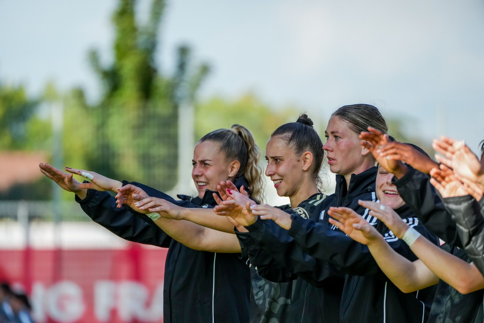 Gruppierung von Frauen in Sportbekleidung, die mit erhobenen Händen in einer Trainingssituation stehen und applaudieren.