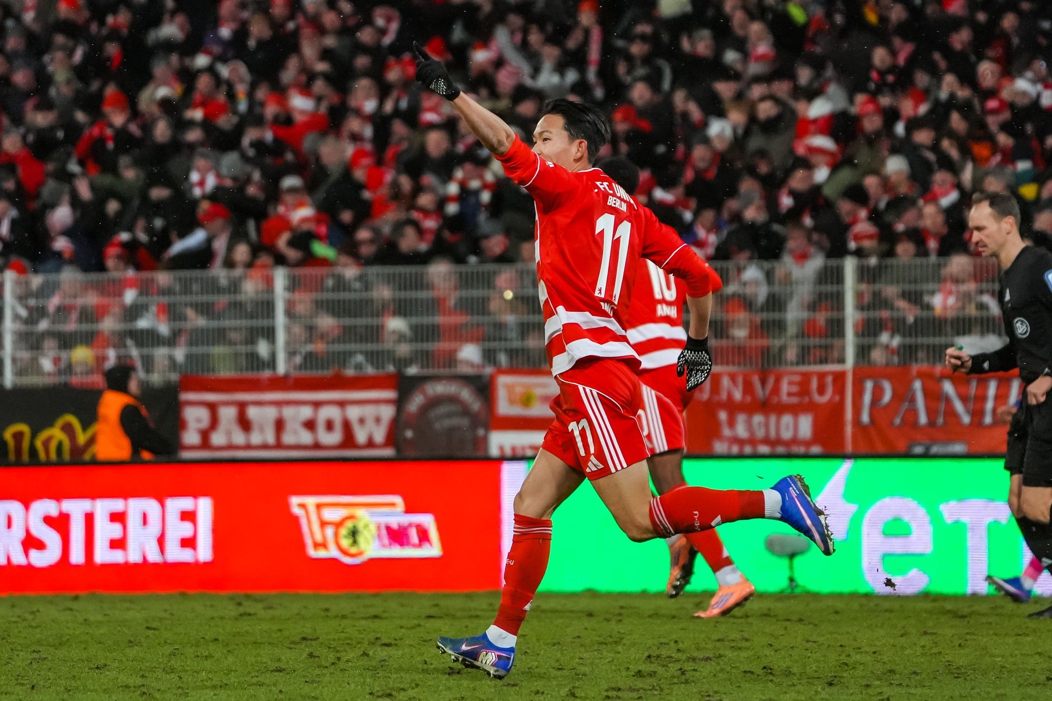 Spieler in rotem Trikot sprintet jubelnd über das Feld, während Zuschauer im Hintergrund feiern.