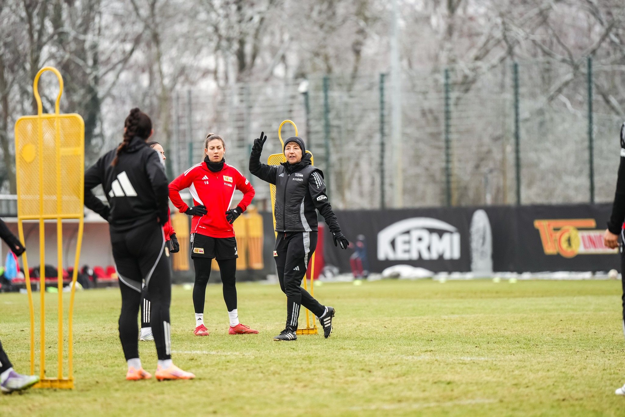 Training der Frauenmannschaft auf dem Platz, mit Trainerin und Spielerinnen in Sportkleidung. Frostige Bedingungen sind sichtbar.