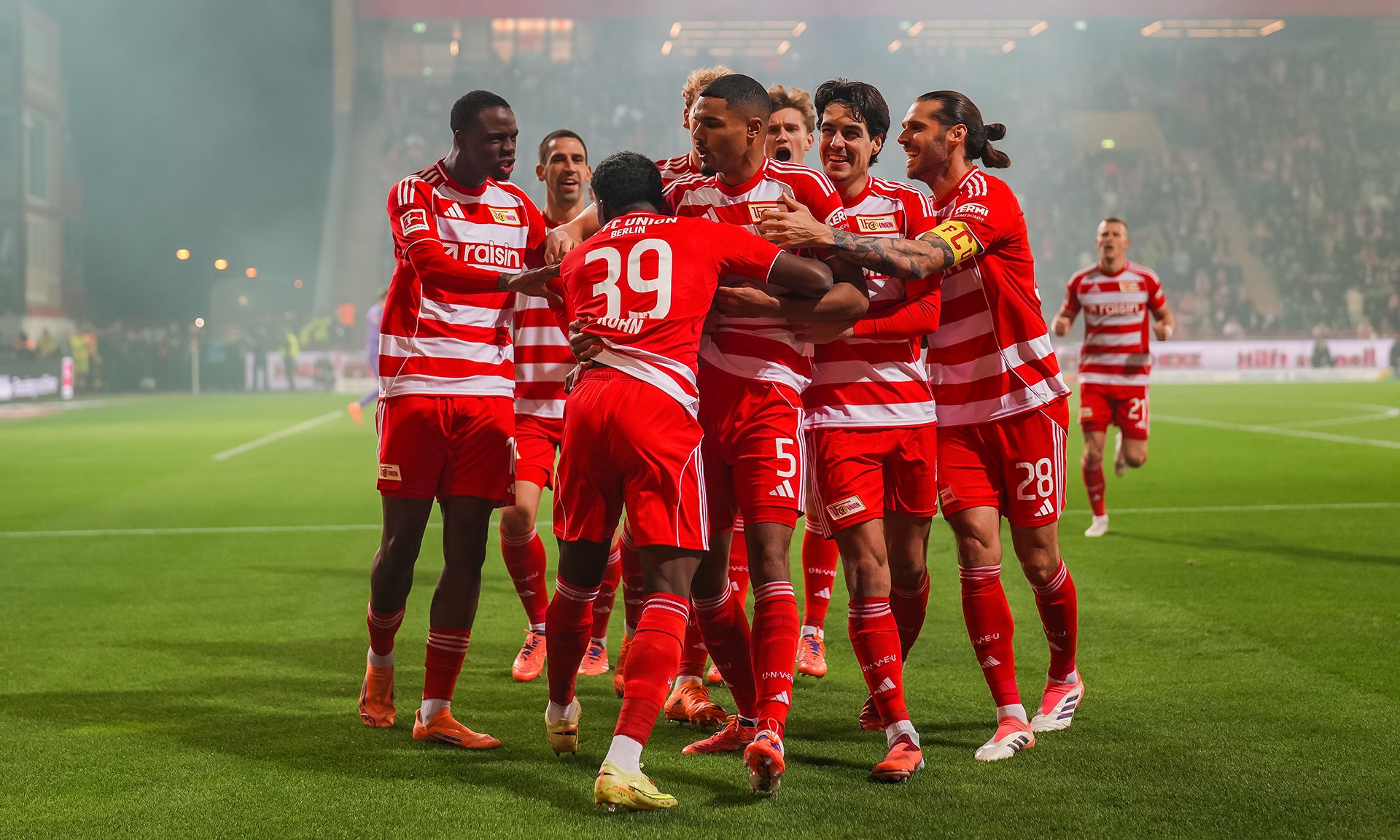 Fußballmannschaft in roten Trikots feiert gemeinsam ein Tor auf dem Spielfeld.